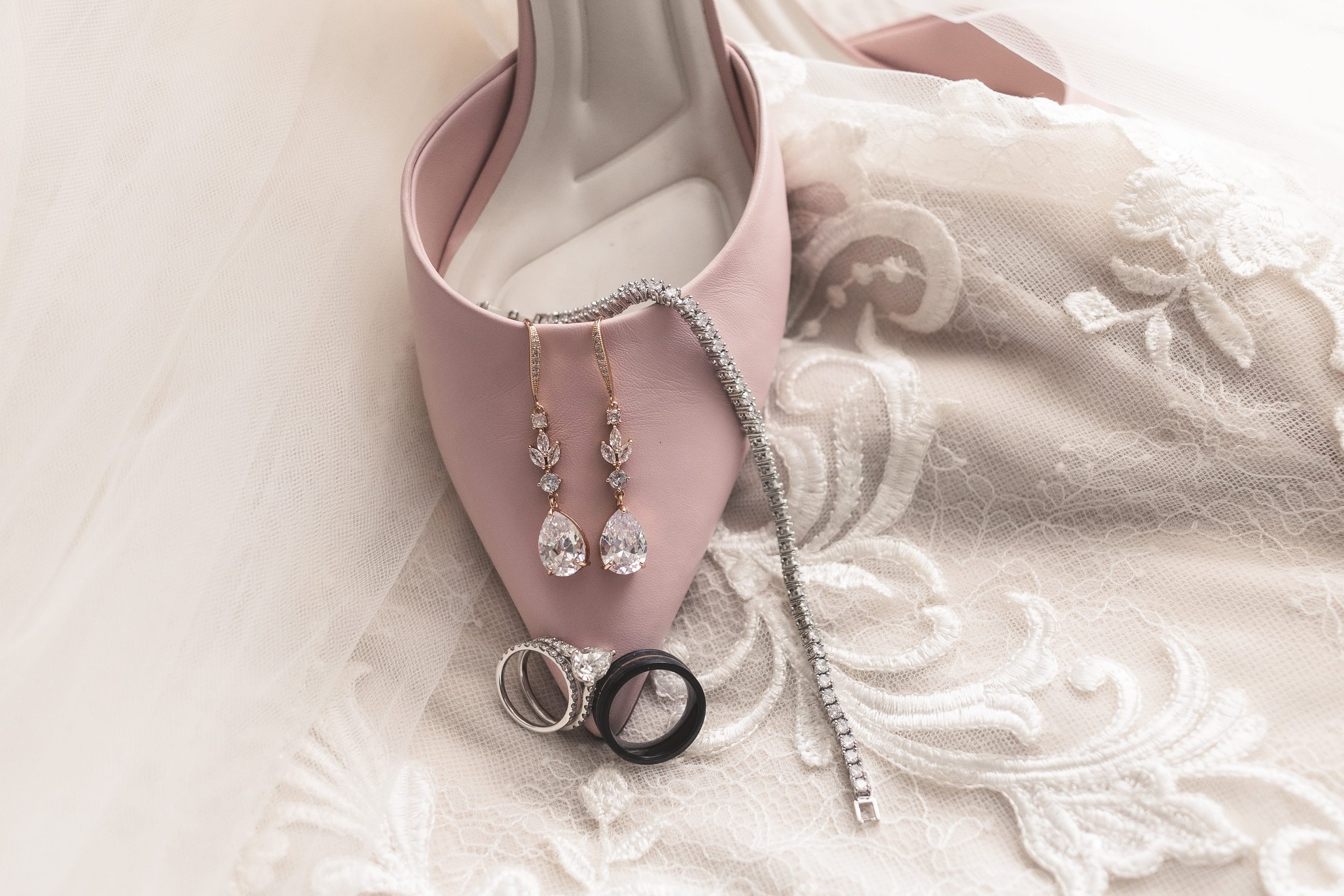 Bridal detail flat lay featuring blush heels, earrings, and jewelry accessories