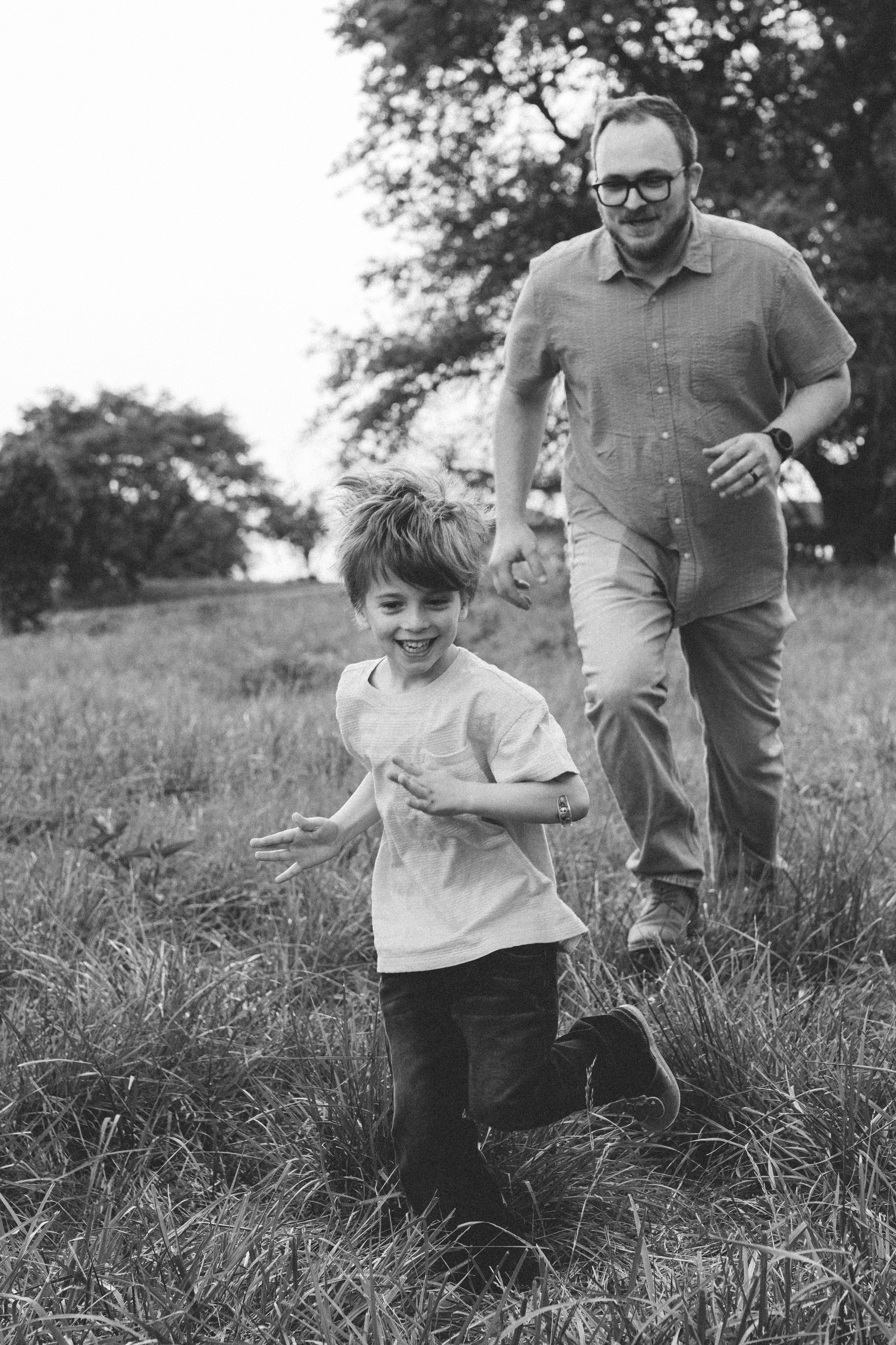Black and white portrait of a father walking hand in hand with his young child in a grassy field
