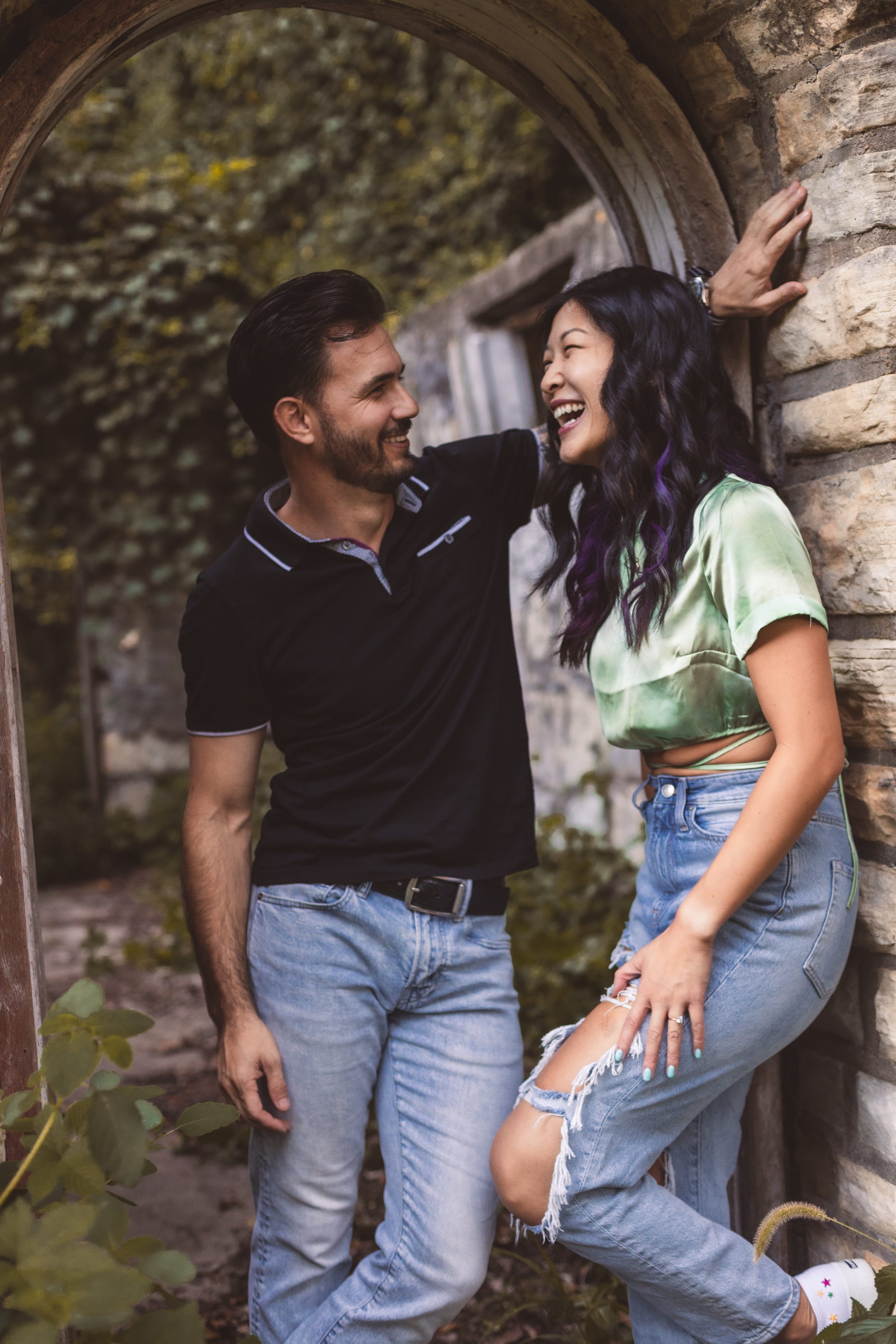 Couple laughing together against a stone and ivy-covered wall during casual couples session