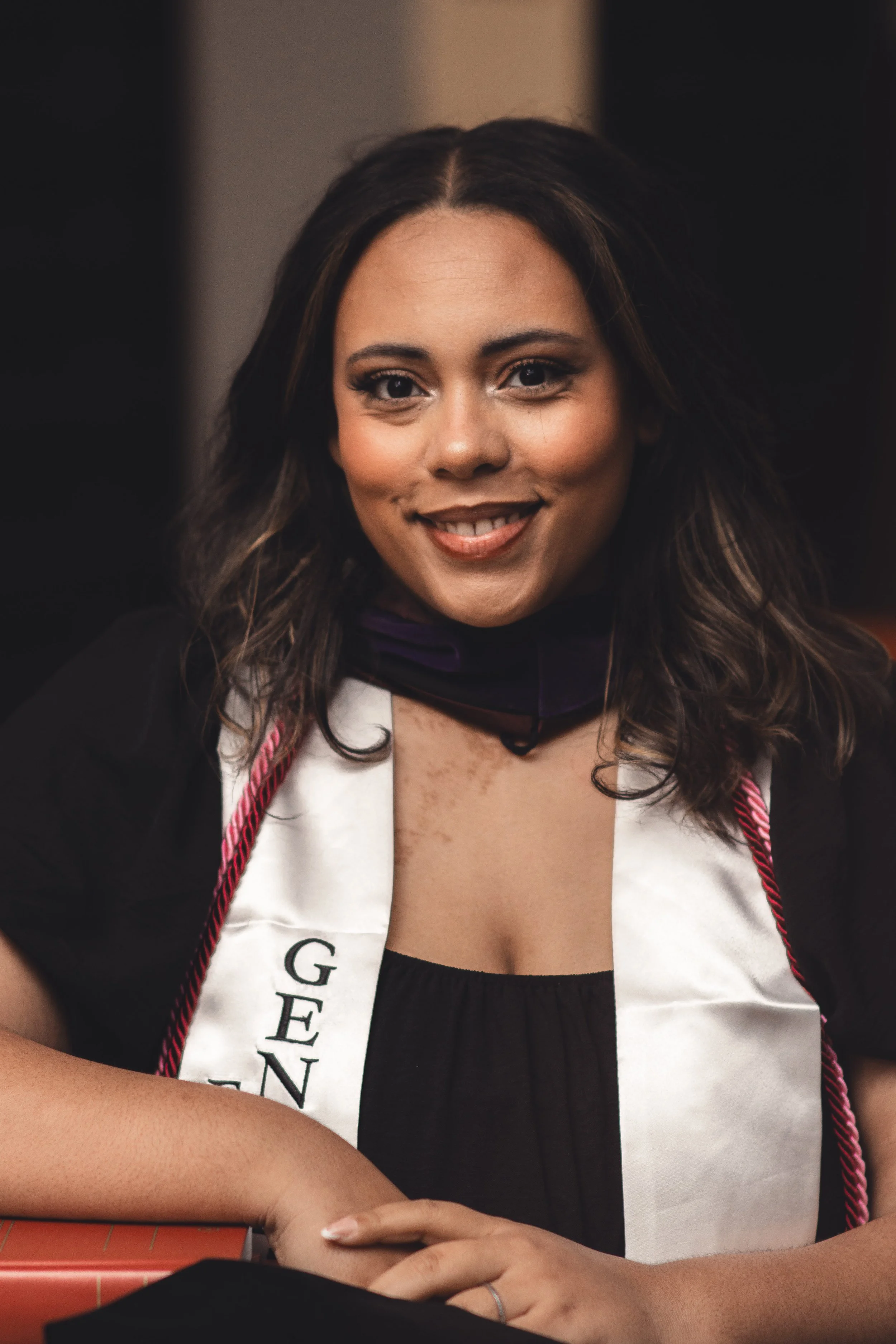 Young woman smiling during her graduation ceremony wearing a white graduation stole and honor cords