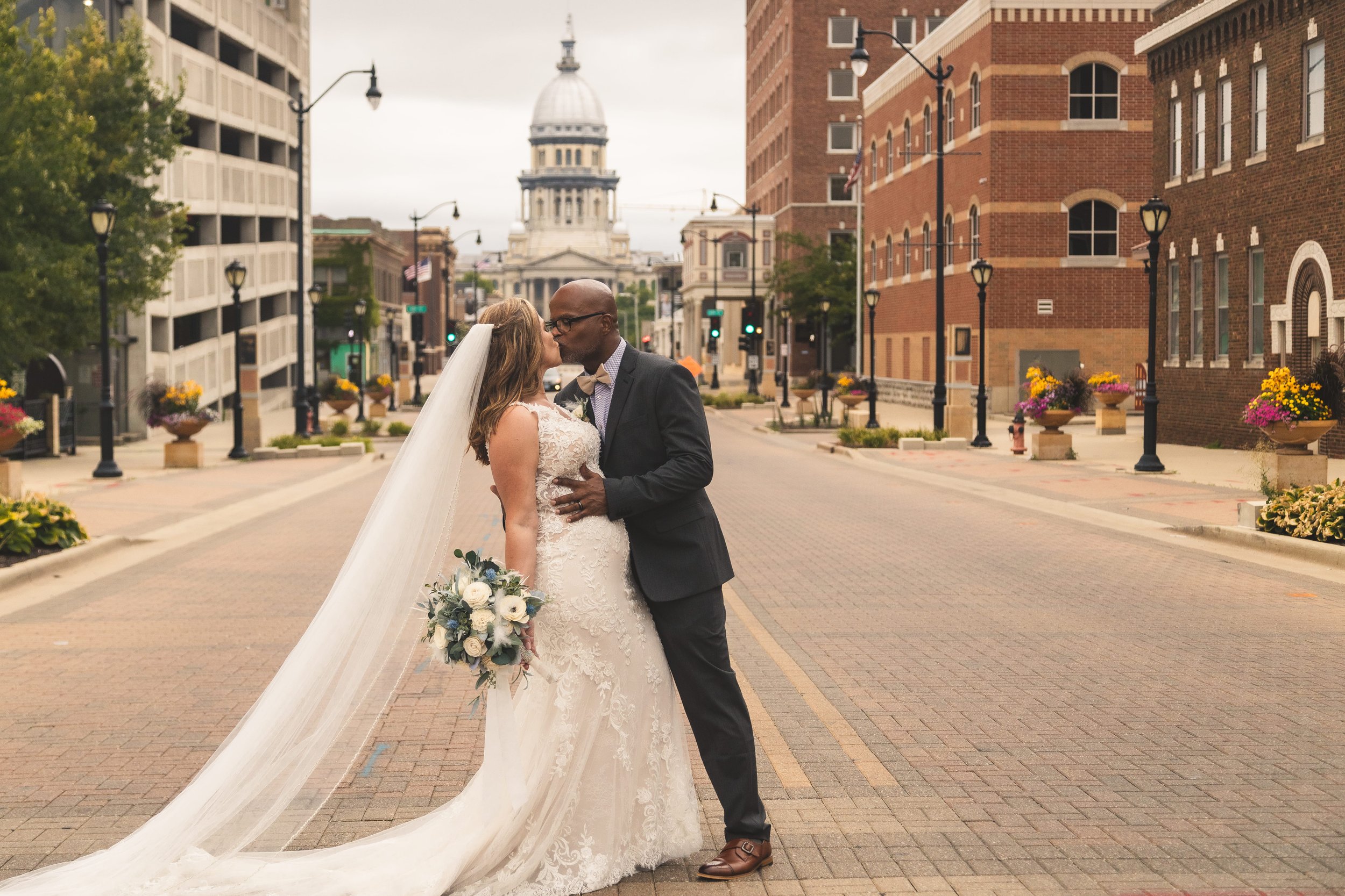 Bride and groom walking hand in hand on a city street with the Illinois State Capitol in the background