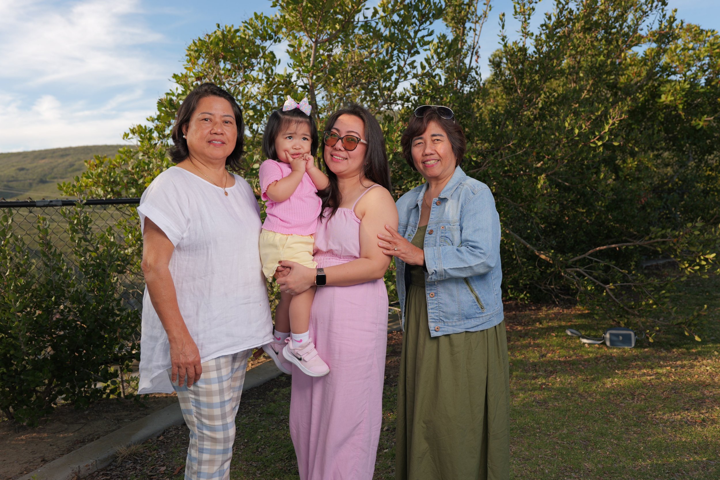 Four women and a young girl standing outdoors in front of trees, smiling at the camera. The youngest girl is being held by one of the women.