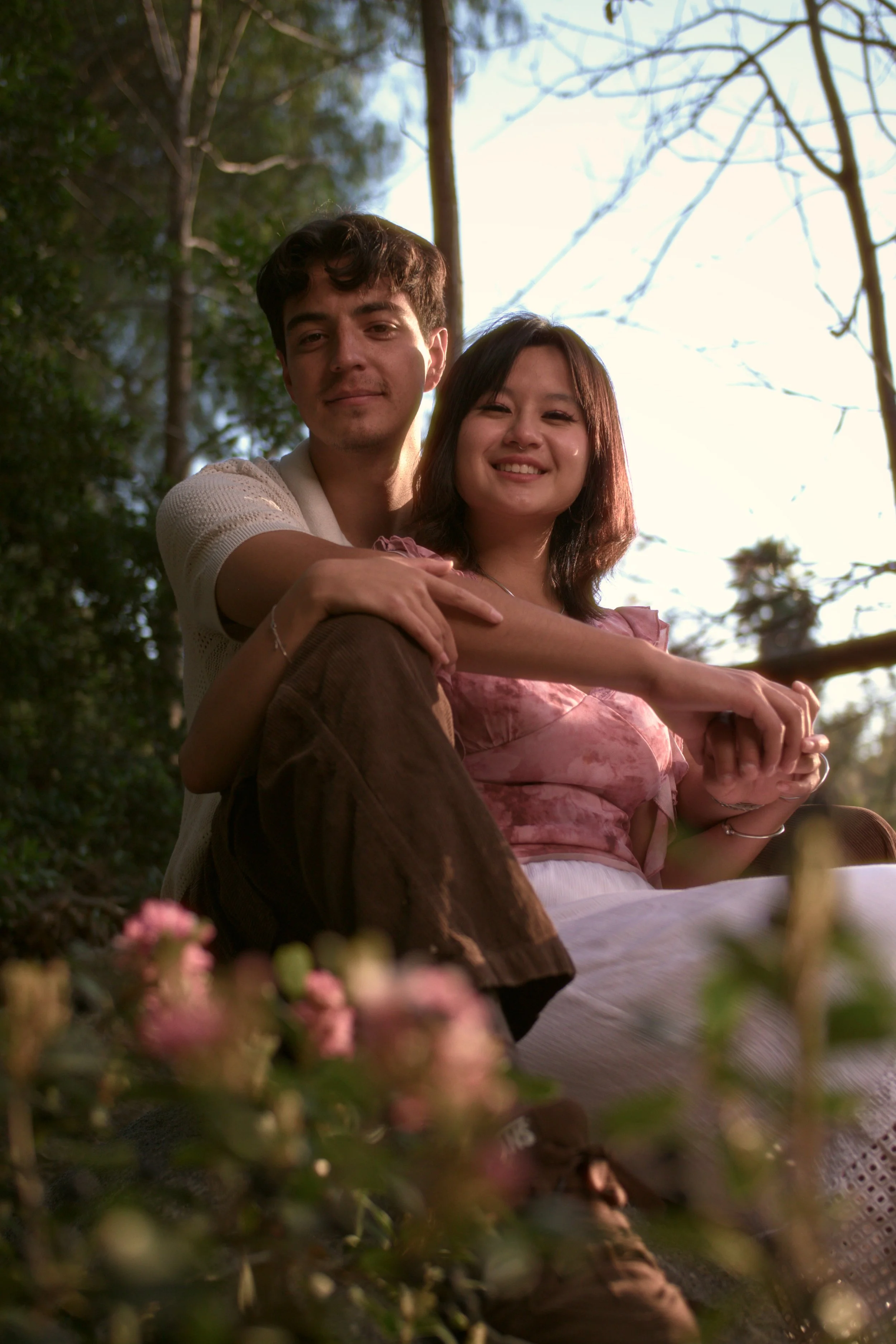 A young man and woman sit together outdoors for a photo, with the man behind the woman, both smiling.