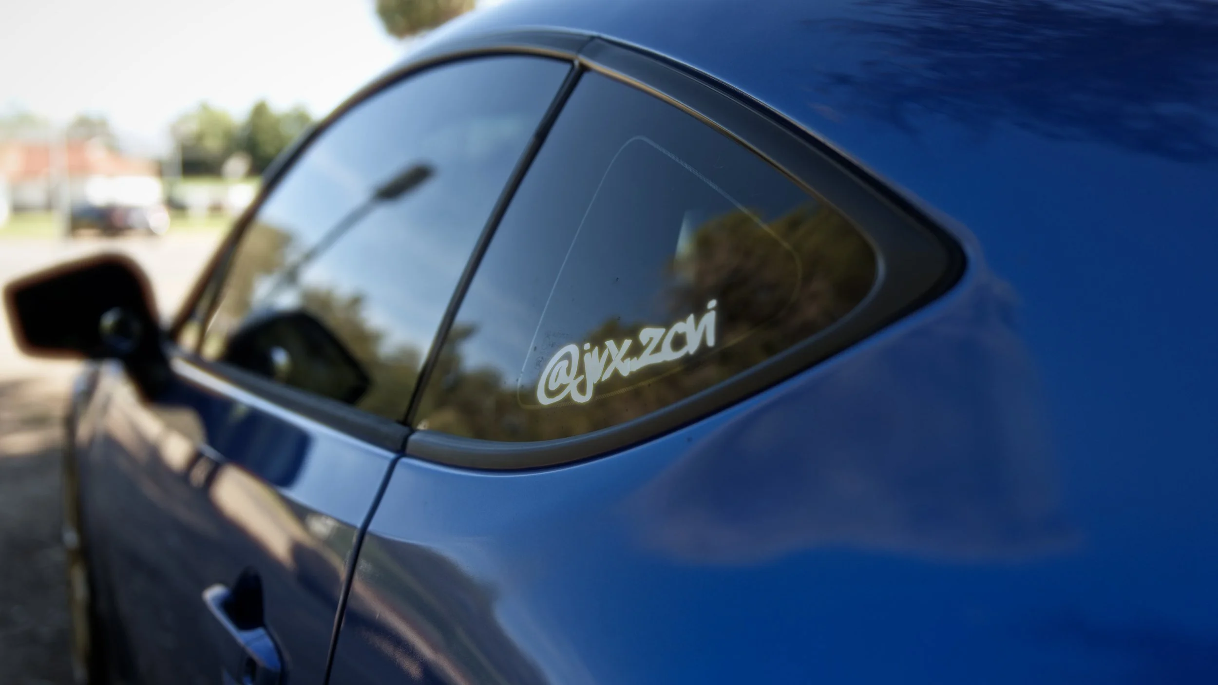 Close-up of a blue car window with a white @jix.zon sticker