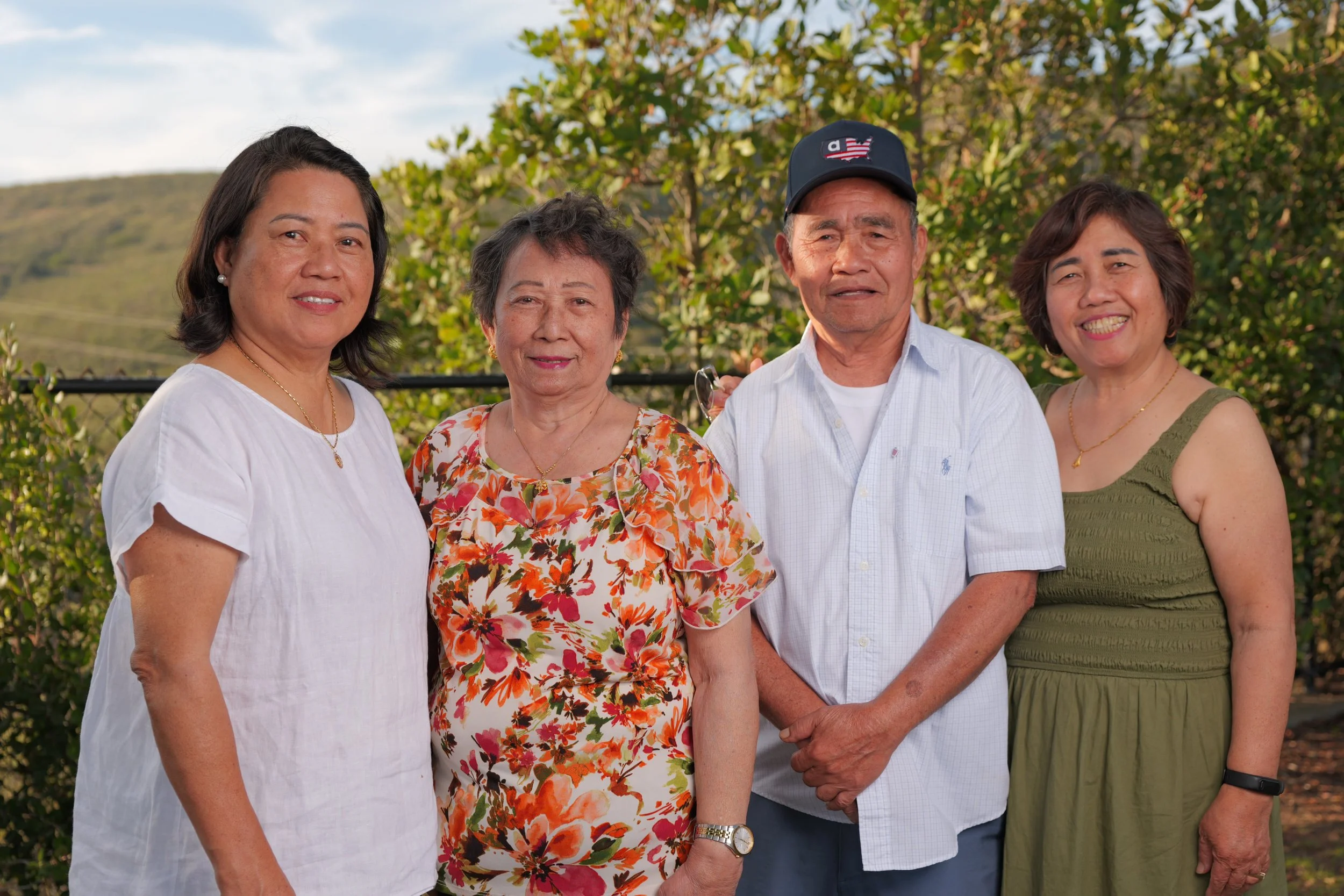 Four adults standing together outdoors with trees and hills in the background, smiling.