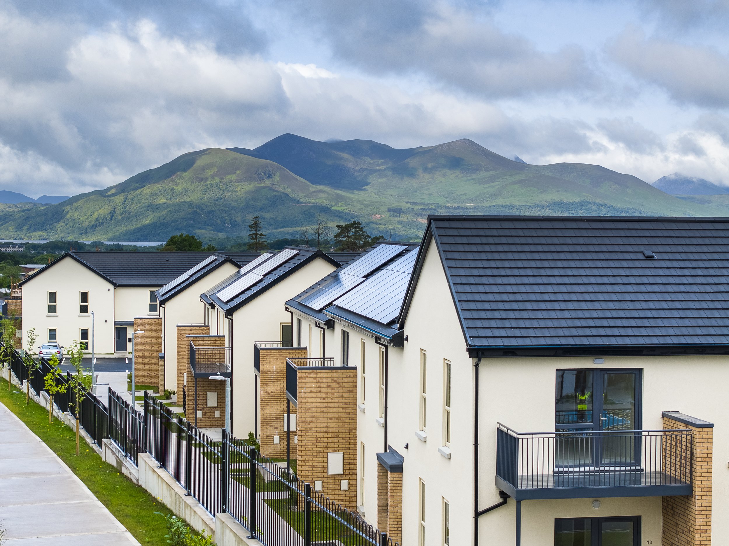 Modern residential buildings with solar panels on the roofs and a mountain range in the background.