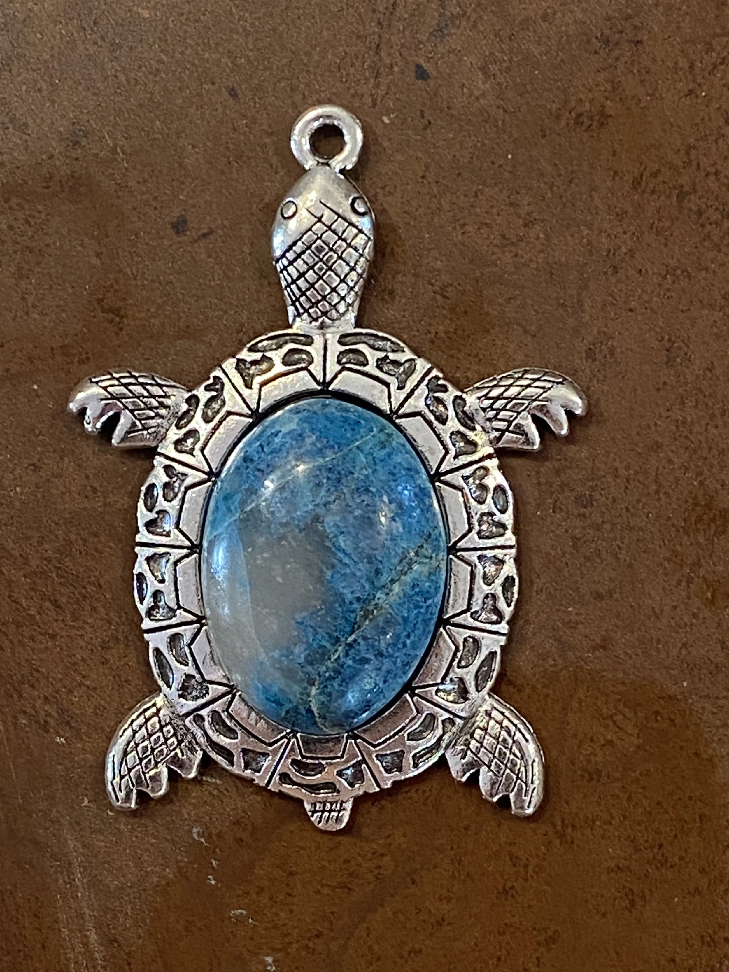 Sea turtle gemstone pendant with polished blue natural stone set in an ornate silver-tone turtle charm. Ocean-inspired jewelry featuring detailed metalwork and a vibrant blue cabochon centerpiece.