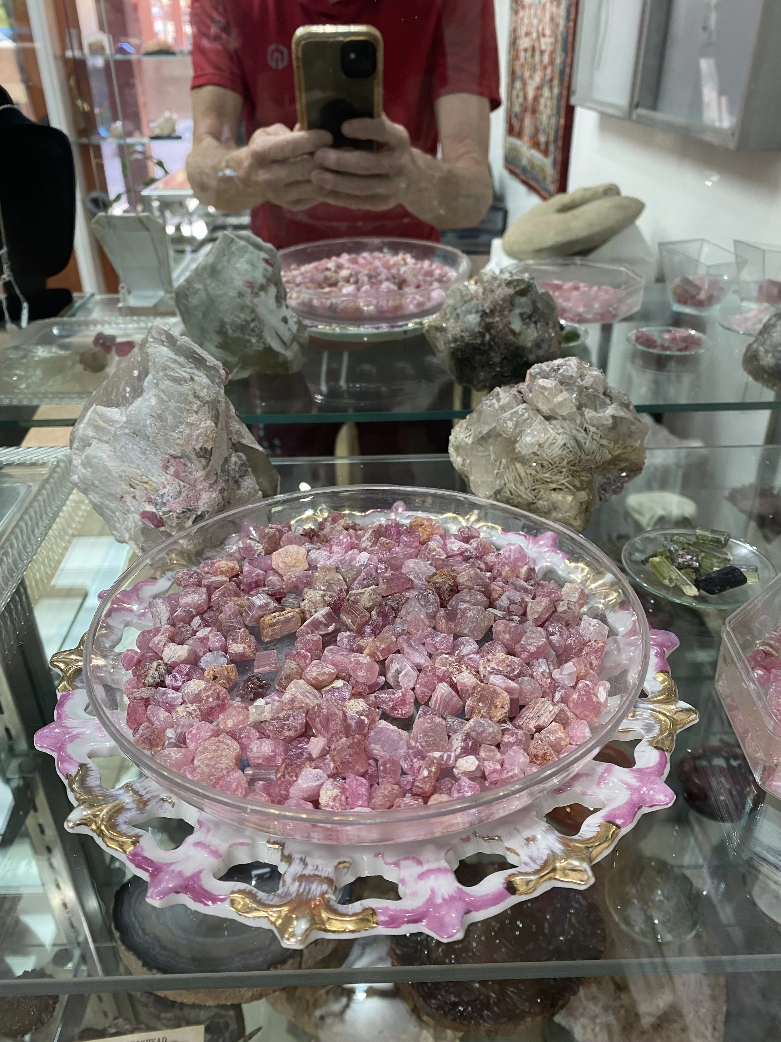 Natural pink tourmaline crystals from the historic Pala Mine in San Diego County, California, displayed in a decorative bowl alongside raw gemstone specimens.