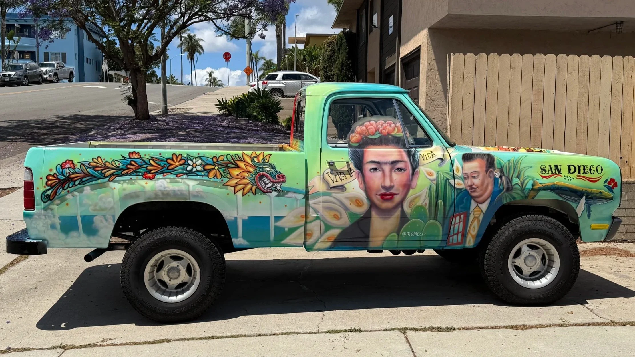 Colorfully painted pickup truck featuring traditional Mexican art, including depictions of Frida Kahlo and Diego Rivera, vibrant flowers, and a dragon, with the words "Viva La Vida" and "San Diego".