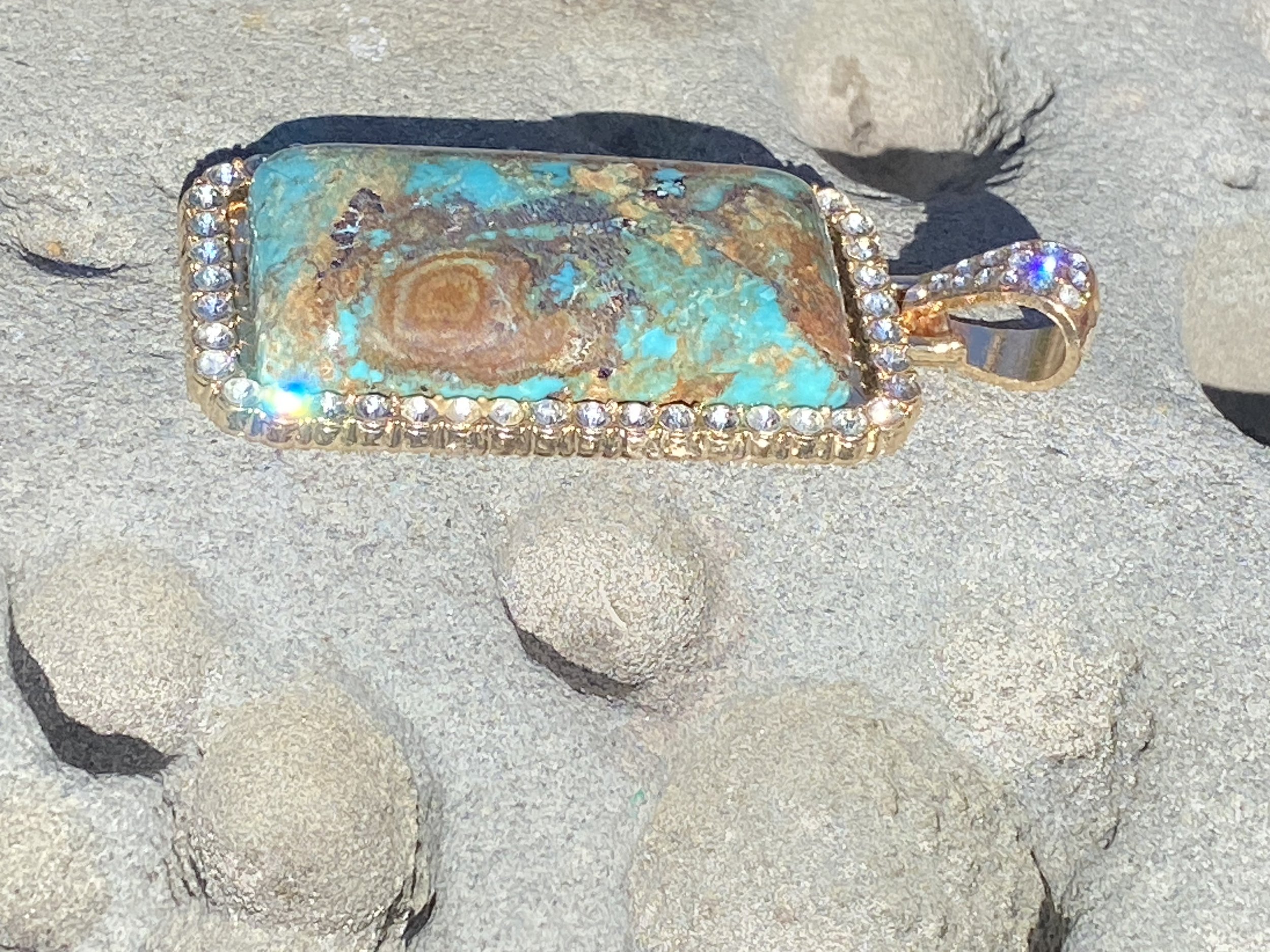 Natural turquoise pendant with vivid blue and brown matrix stone set in a gold-tone frame with clear accent stones.