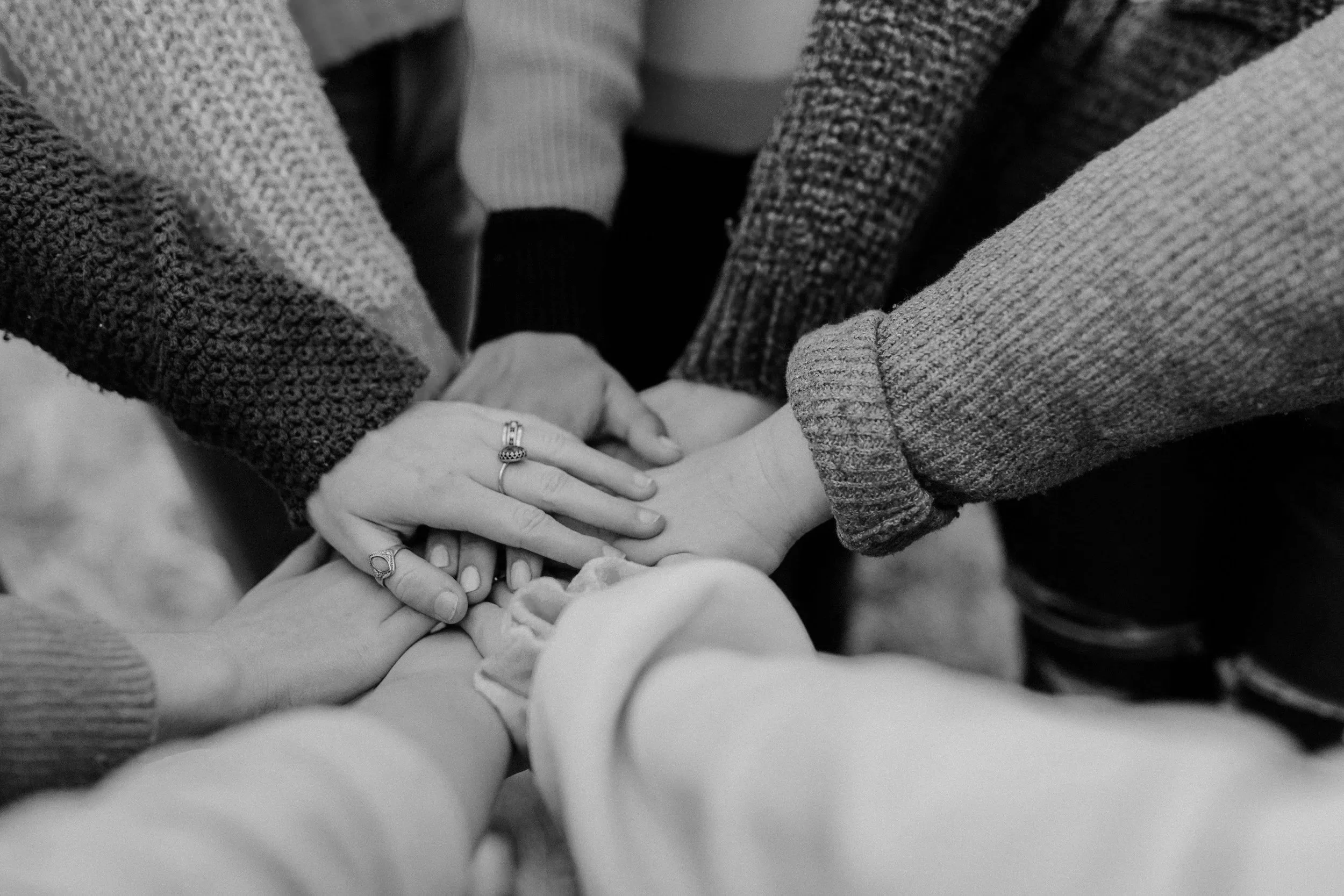 Multiple hands stacked together, some with rings, in a gesture of unity or support.