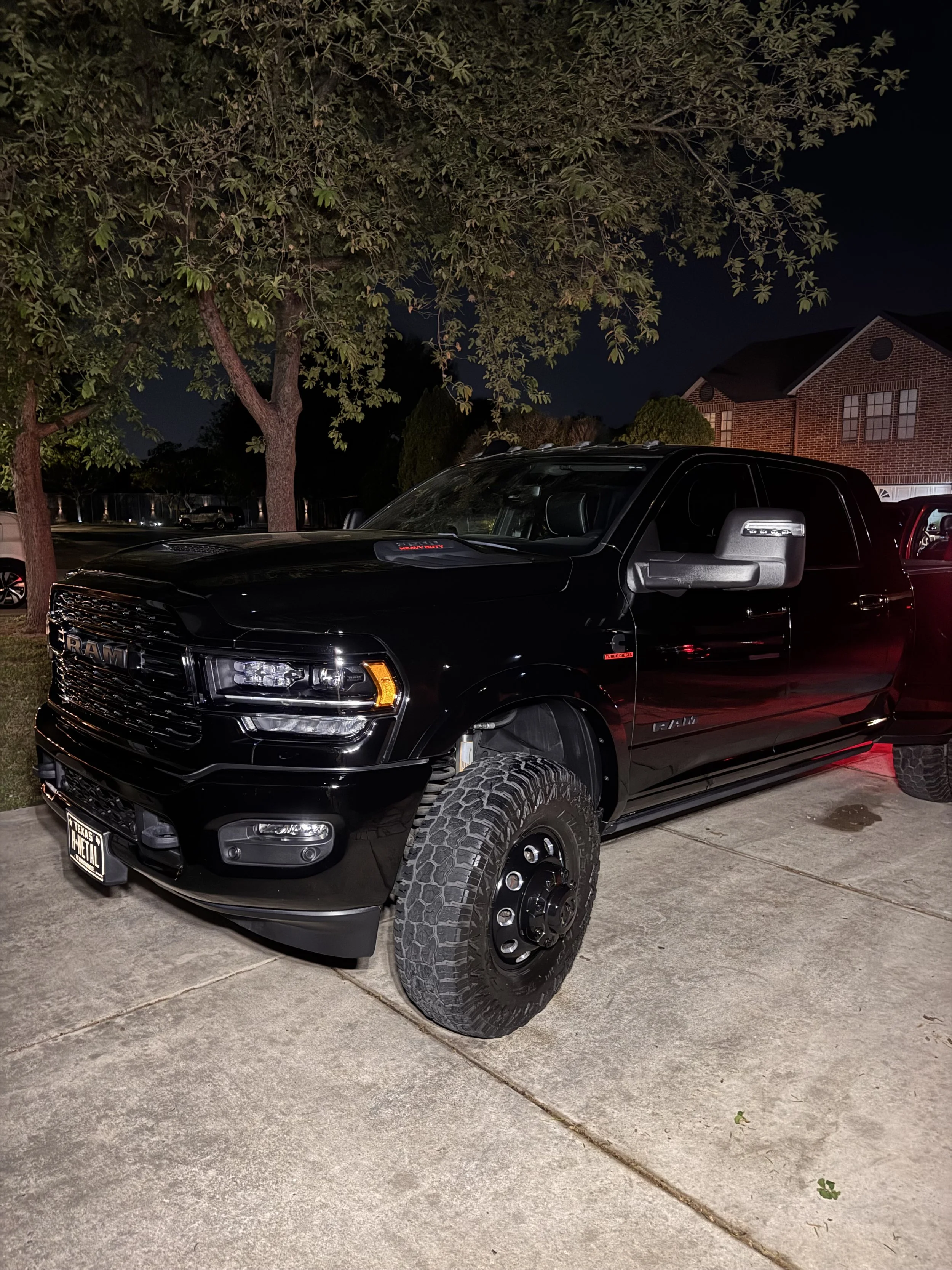 A black RAM pickup truck parked on a driveway at night with a house and trees in the background.