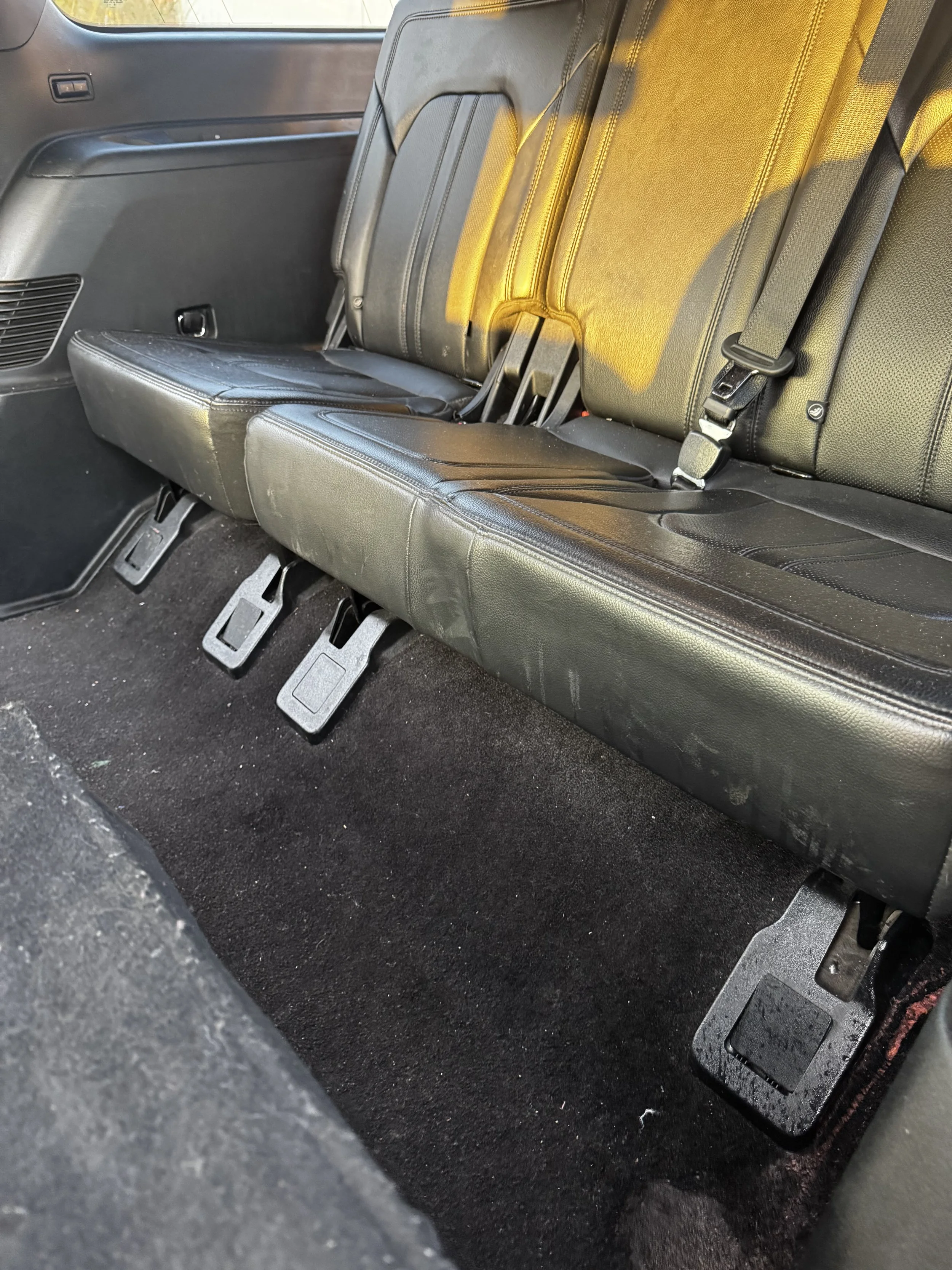The rear interior of a vehicle showing black leather seats, black carpeted floor, and visible seat belts.