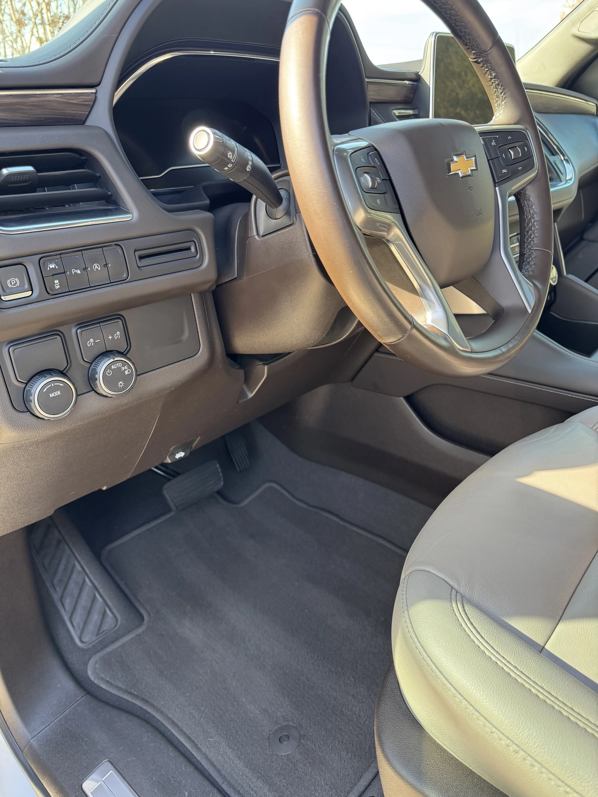 Interior of a Chevrolet vehicle showing the steering wheel with Chevrolet emblem, dashboard, air vents, control buttons, and beige seat.