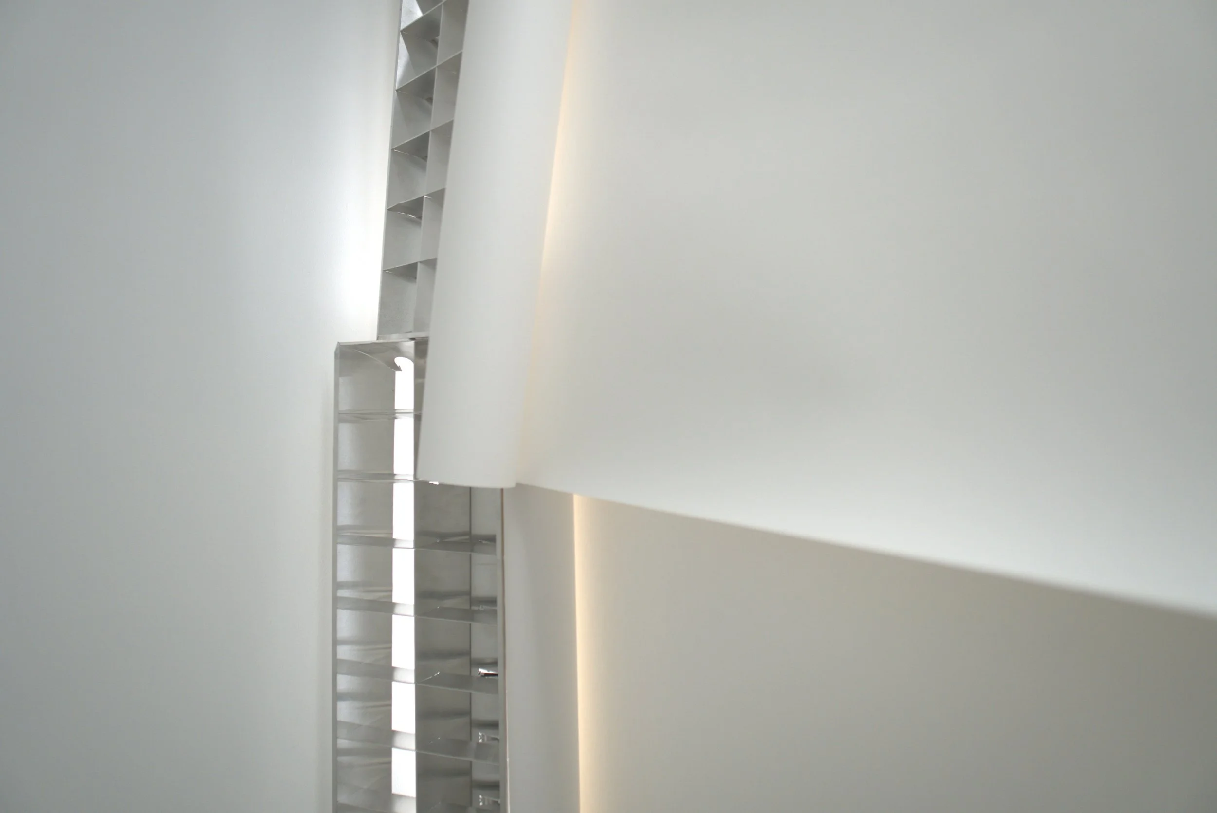 Vista de una pared blanca con un estante de color gris claro en forma de escalera en una habitación moderna y minimalista.