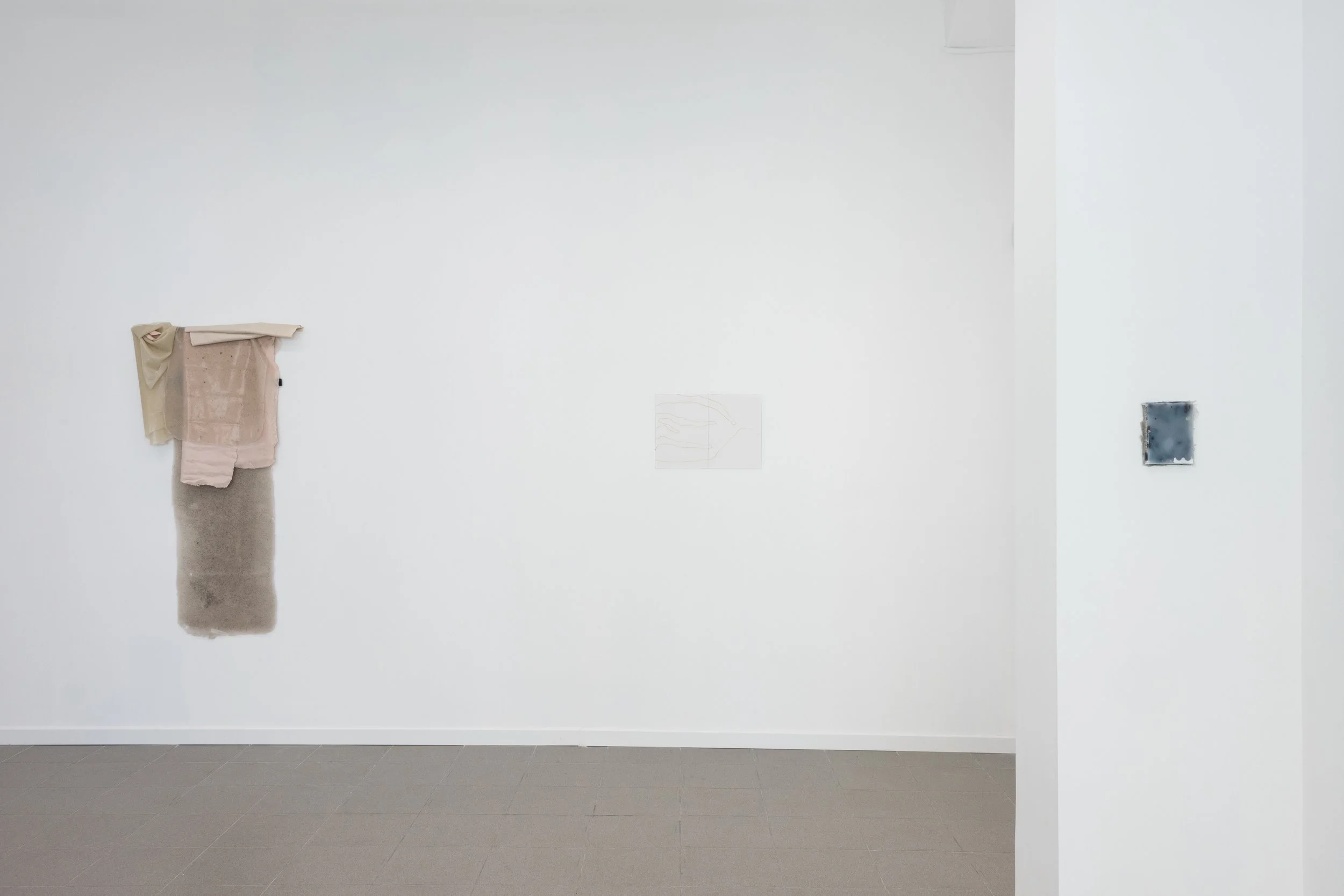Galería de arte con varias obras minimalistas en paredes blancas y suelo de baldosas grises.