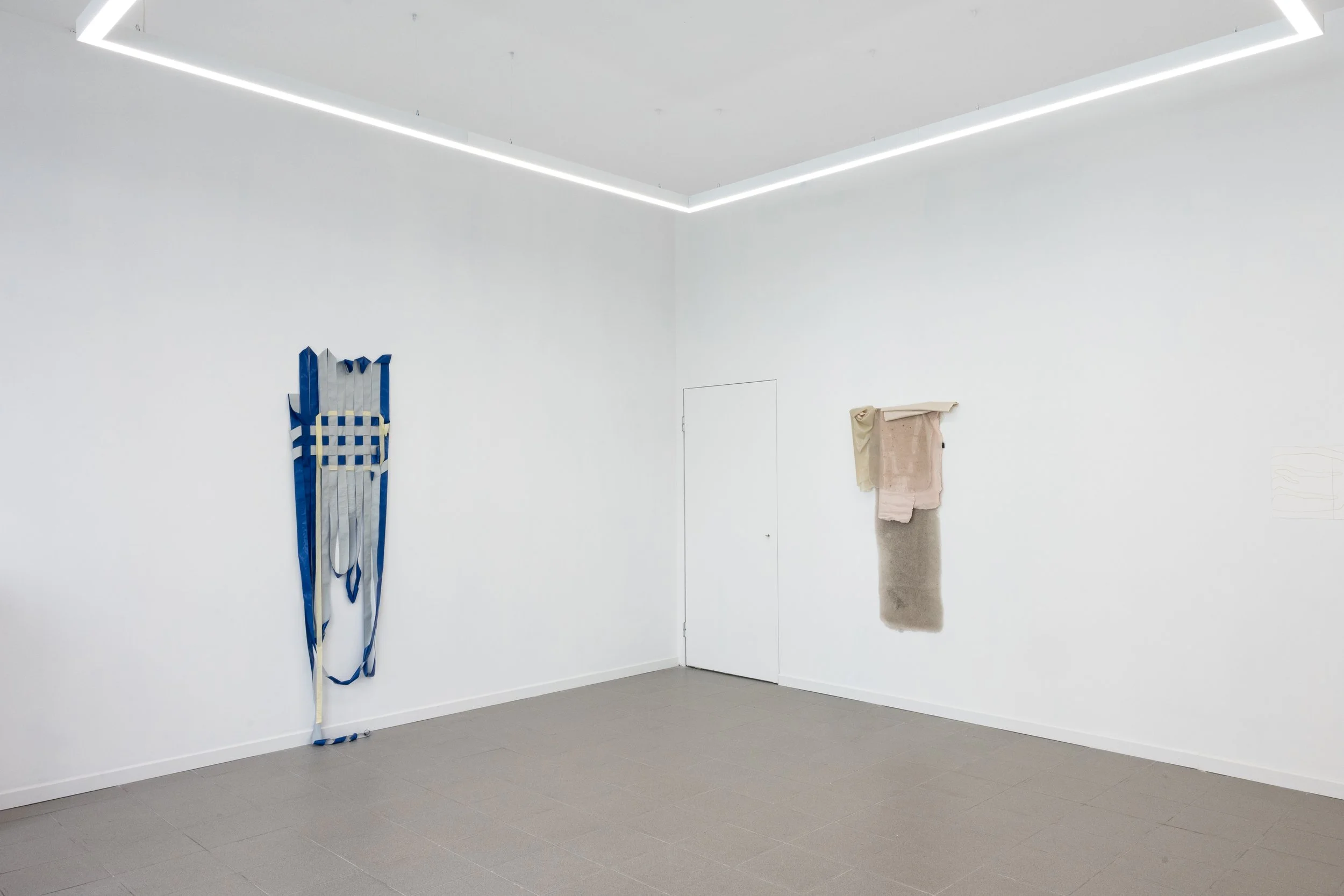 Sala de exposición con obras de arte en las paredes, decoración minimalista, paredes blancas, techo con iluminación lineal, suelo gris, apareció varias piezas de arte en las paredes y una escultura en el suelo.