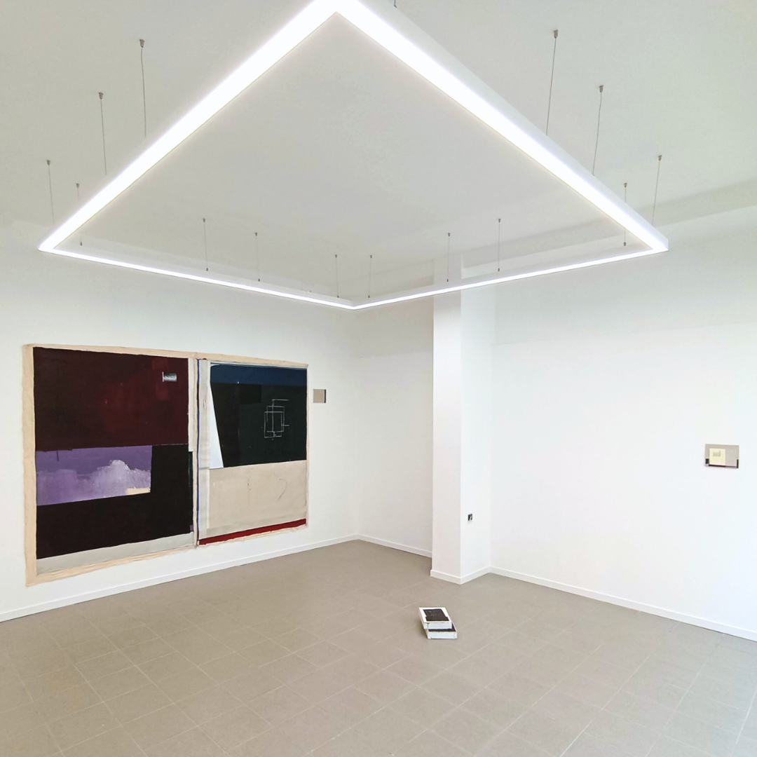 Sala blanca con una pintura abstracta en la pared y un techo con iluminación moderna en forma de cuadrado.
