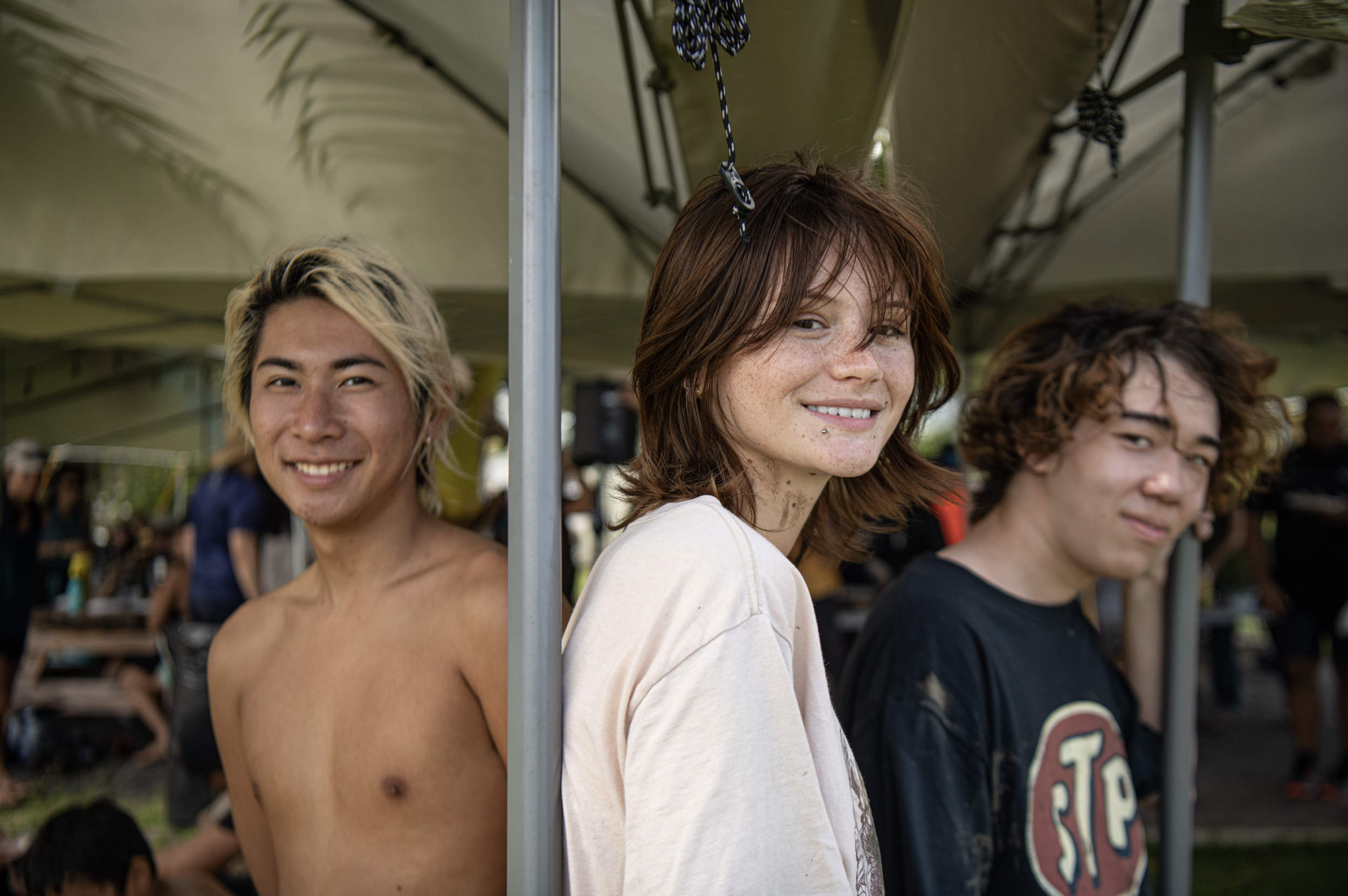 Three young people standing near a tent outdoors, smiling and looking at the camera.