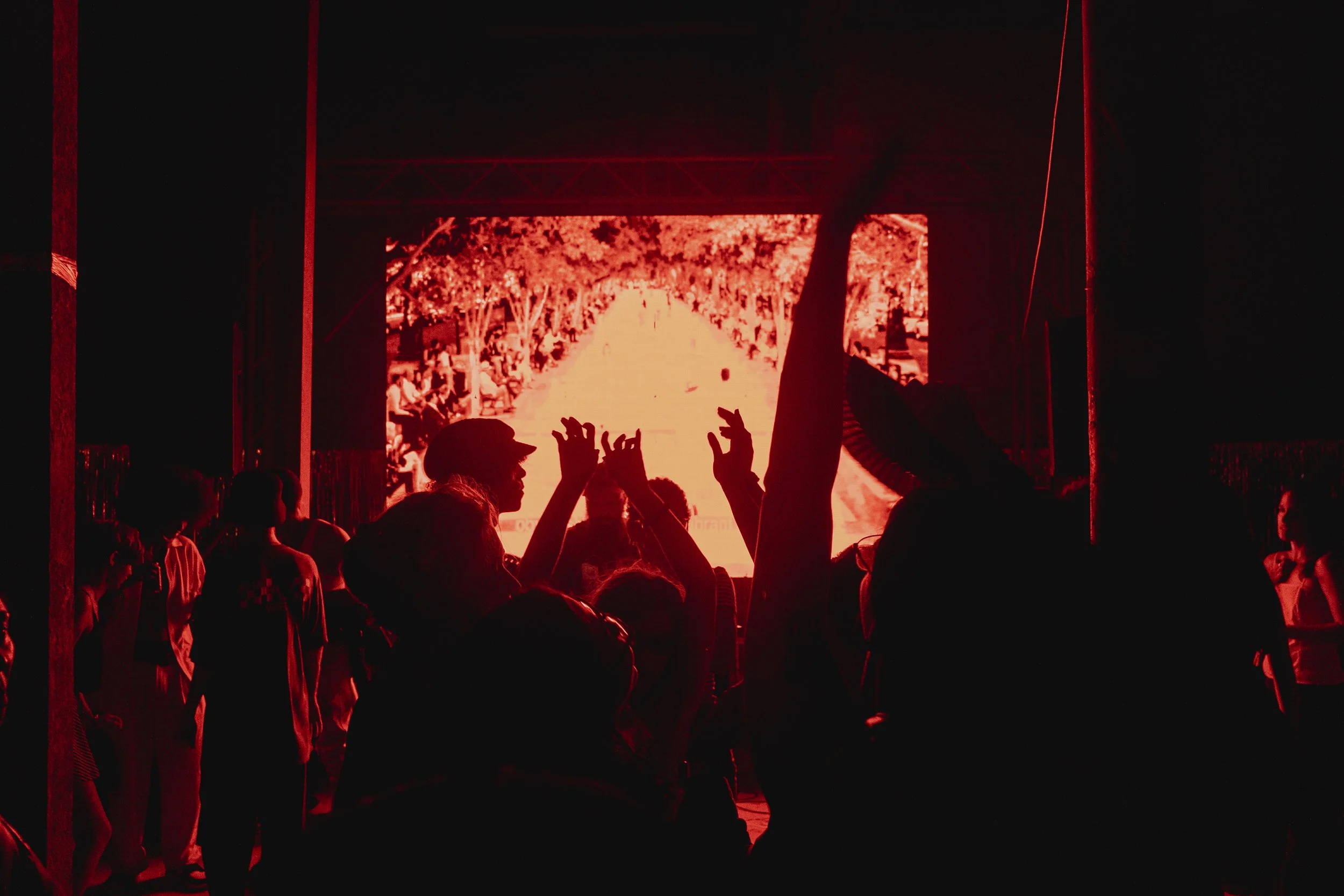 Personas en un concierto con una pantalla grande que muestra imágenes en color rojo, en un ambiente oscuro.