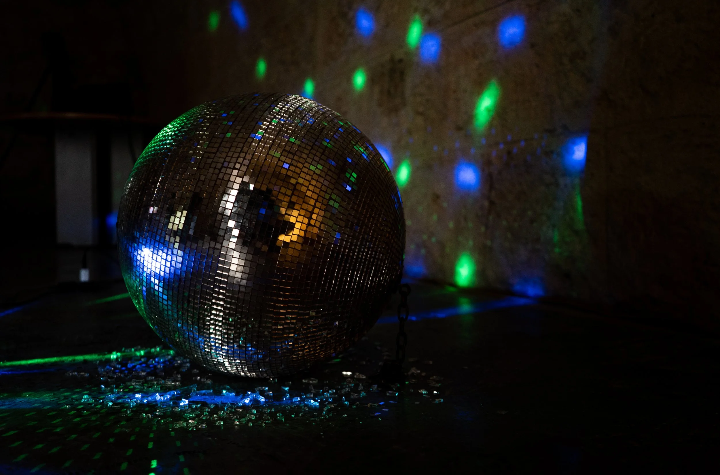 Espejo de bola decorativa en un entorno oscuro, proyectando luces verdes, azules y blancas sobre una superficie y en la pared.