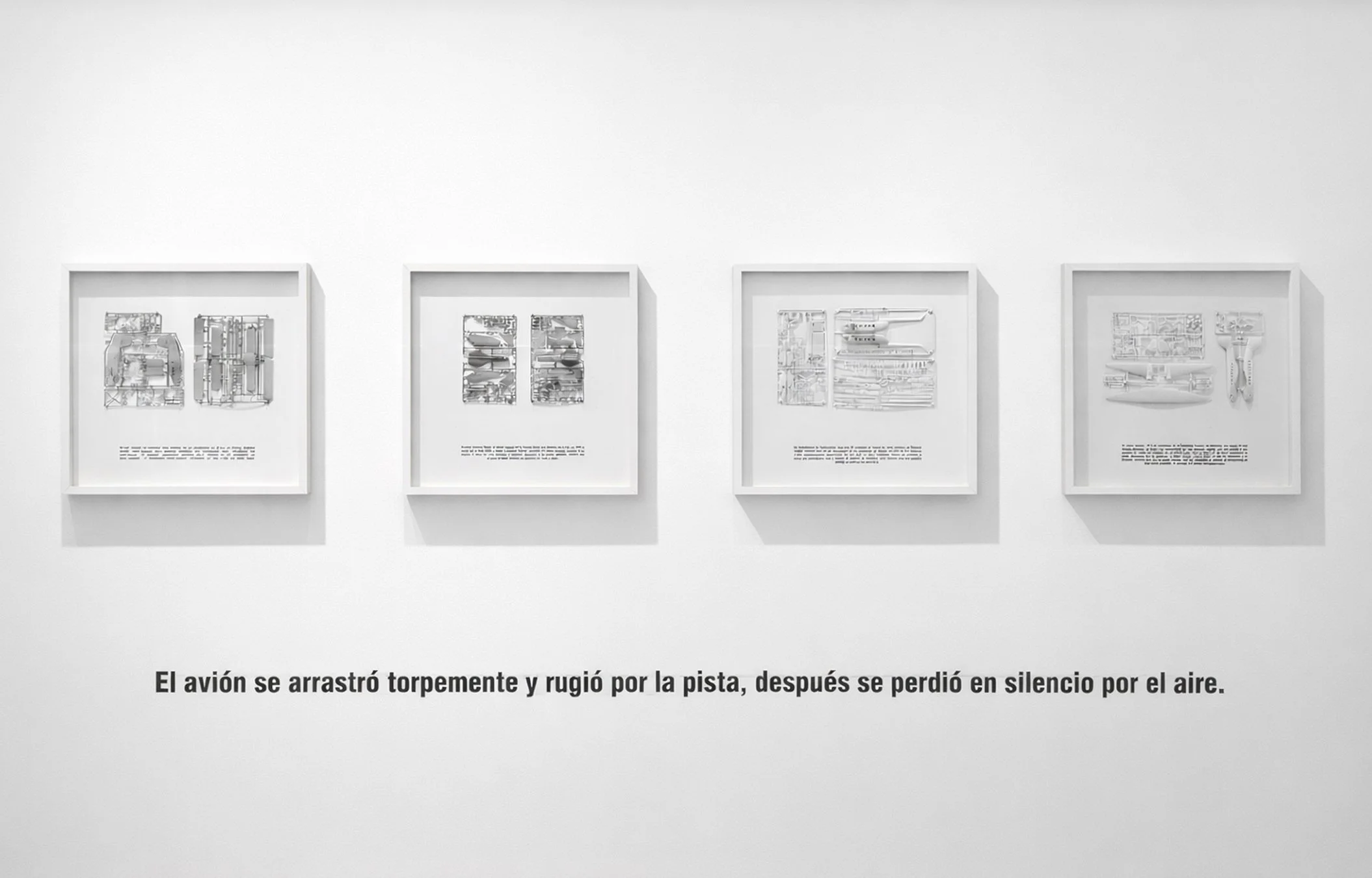 Cuatro cuadros enmarcados en una pared blanca, contienen dibujos y textos en un estilo técnico o esquemático, en una exposición o galería de arte.