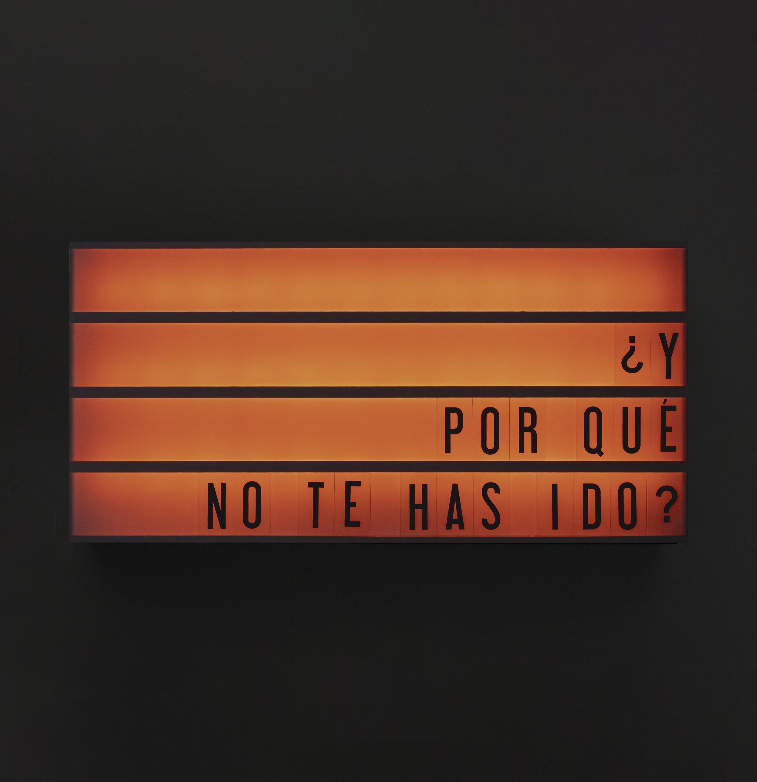Luz de cartel con letras rojas y negras sobre fondo negro y naranja, que dice: ¿Y POR QUÉ NO TE HAS IDO?