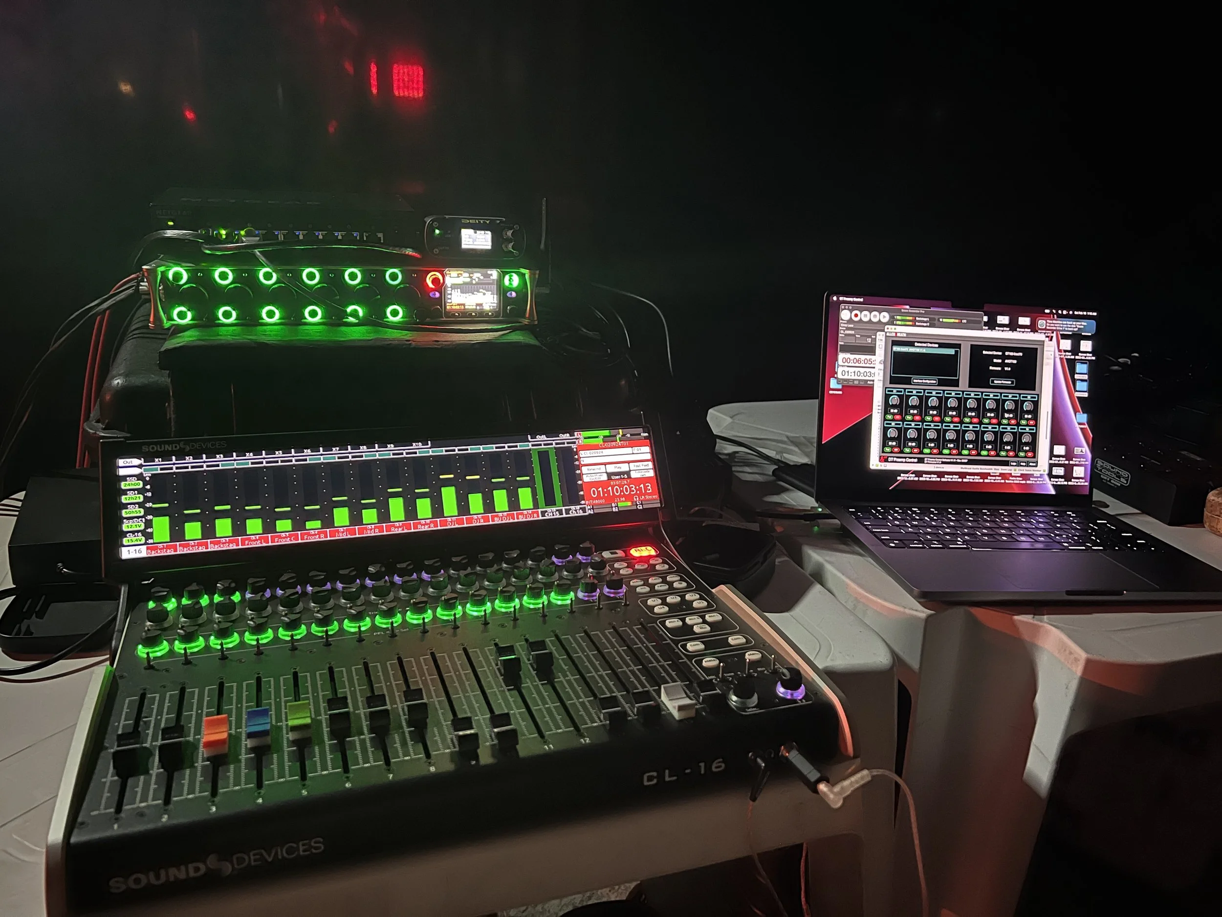 DJ equipment setup with a mixing console, a laptop, and additional audio gear, illuminated with green and purple lights.