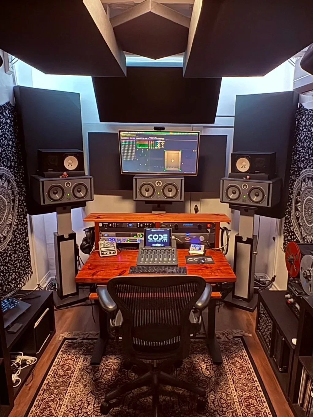 A professional recording & mixing studio with a computer monitor, audio equipment, and studio monitors, set up in a well-organized space with acoustic panels, a wooden desk, and a rug. Dolby Atmos.