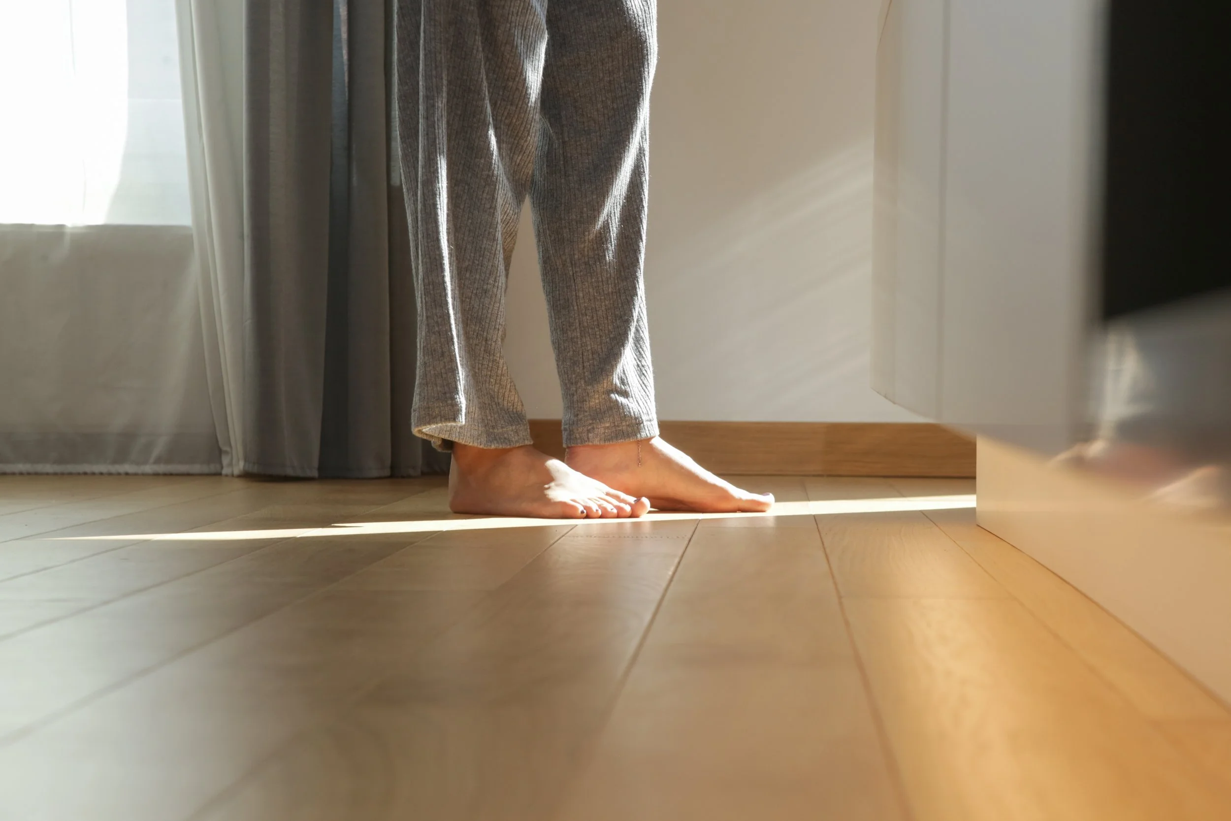 Bare feet on warm hardwood floor with morning sunlight streaming across the room