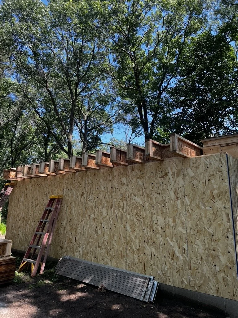 Construction site with a wooden wall, ladders, and tree-covered background.