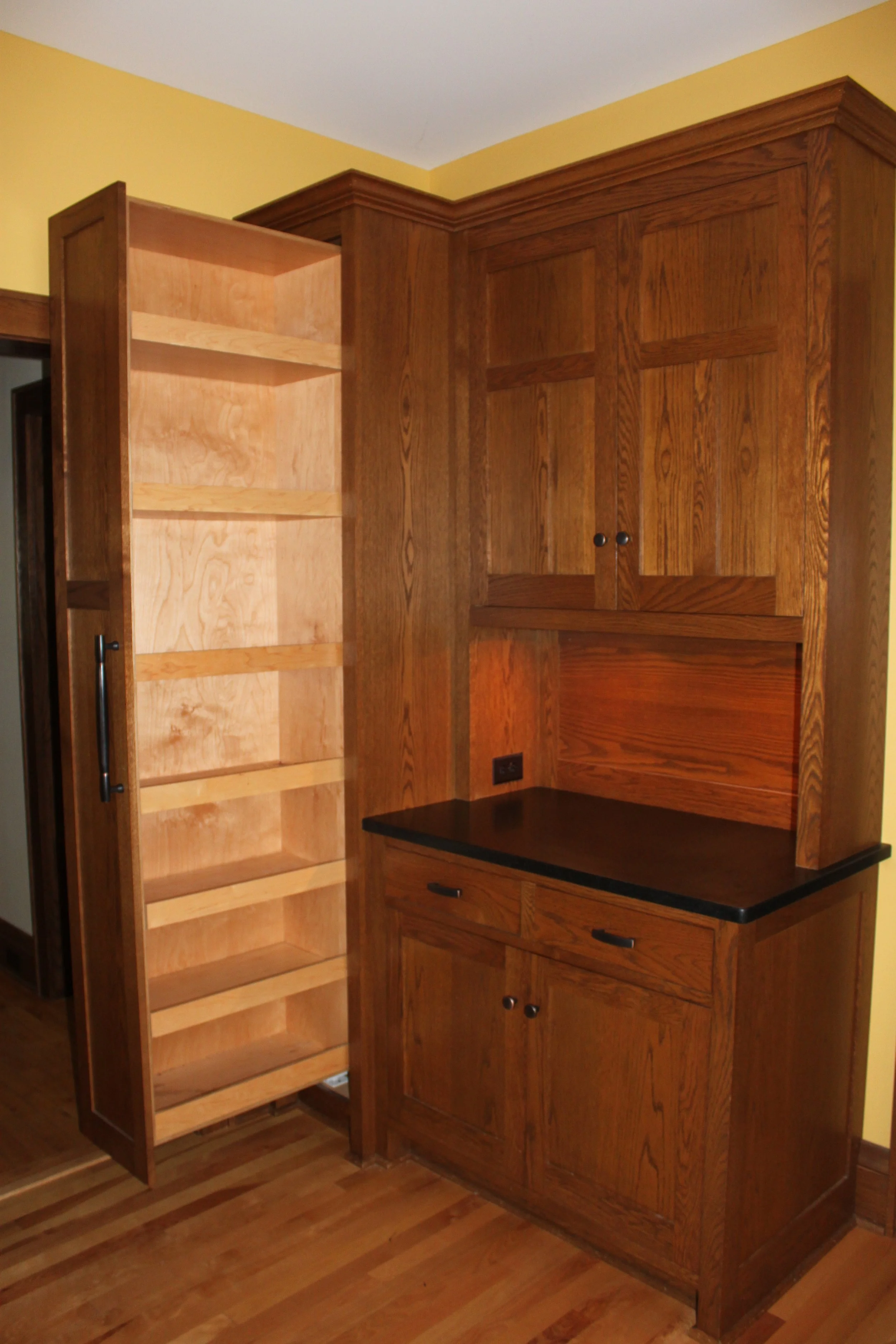 Wooden kitchen cabinet with open shelves and drawers, black countertop, and yellow wall in the background.