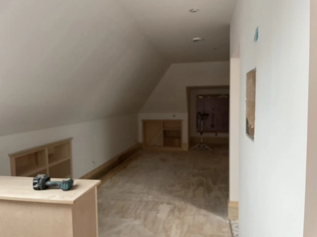 An attic room under construction with electrical tools on a wooden surface, built-in shelves, and a small table.