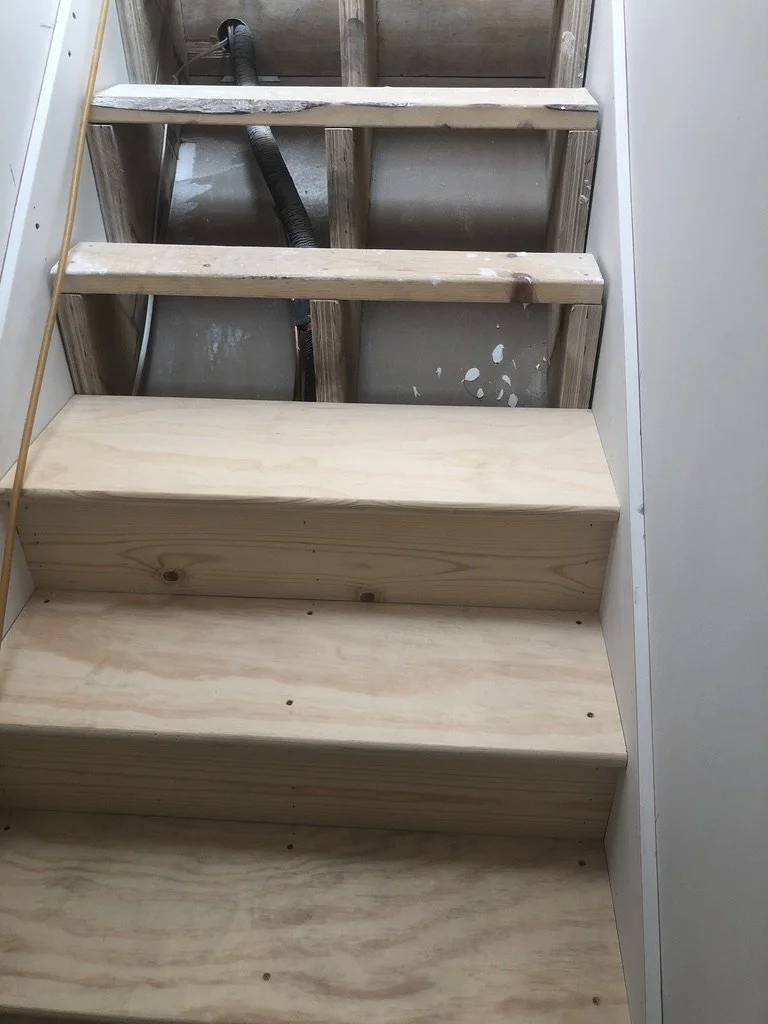Unfinished wooden staircase with three visible steps, no handrails, and exposed framing and wiring in the background.