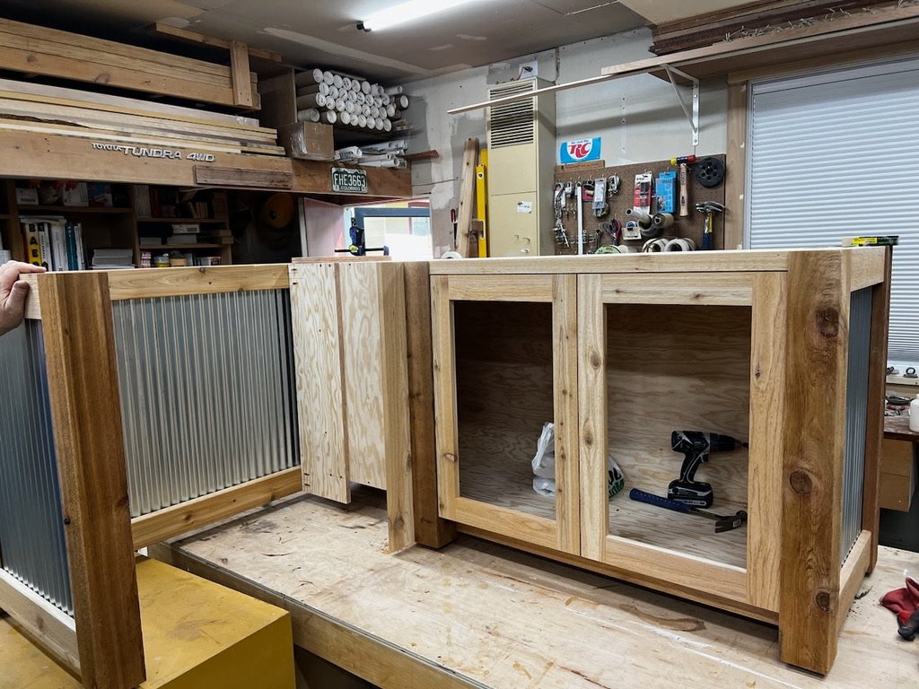 Wooden cabinet or countertop in a workshop, with metal and wood materials, tools, and supplies in the background.