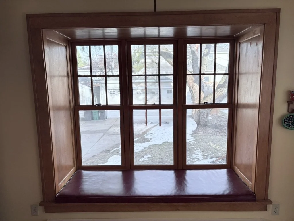 Wooden window seat with a large window showing an outdoor scene with a tree and snow.