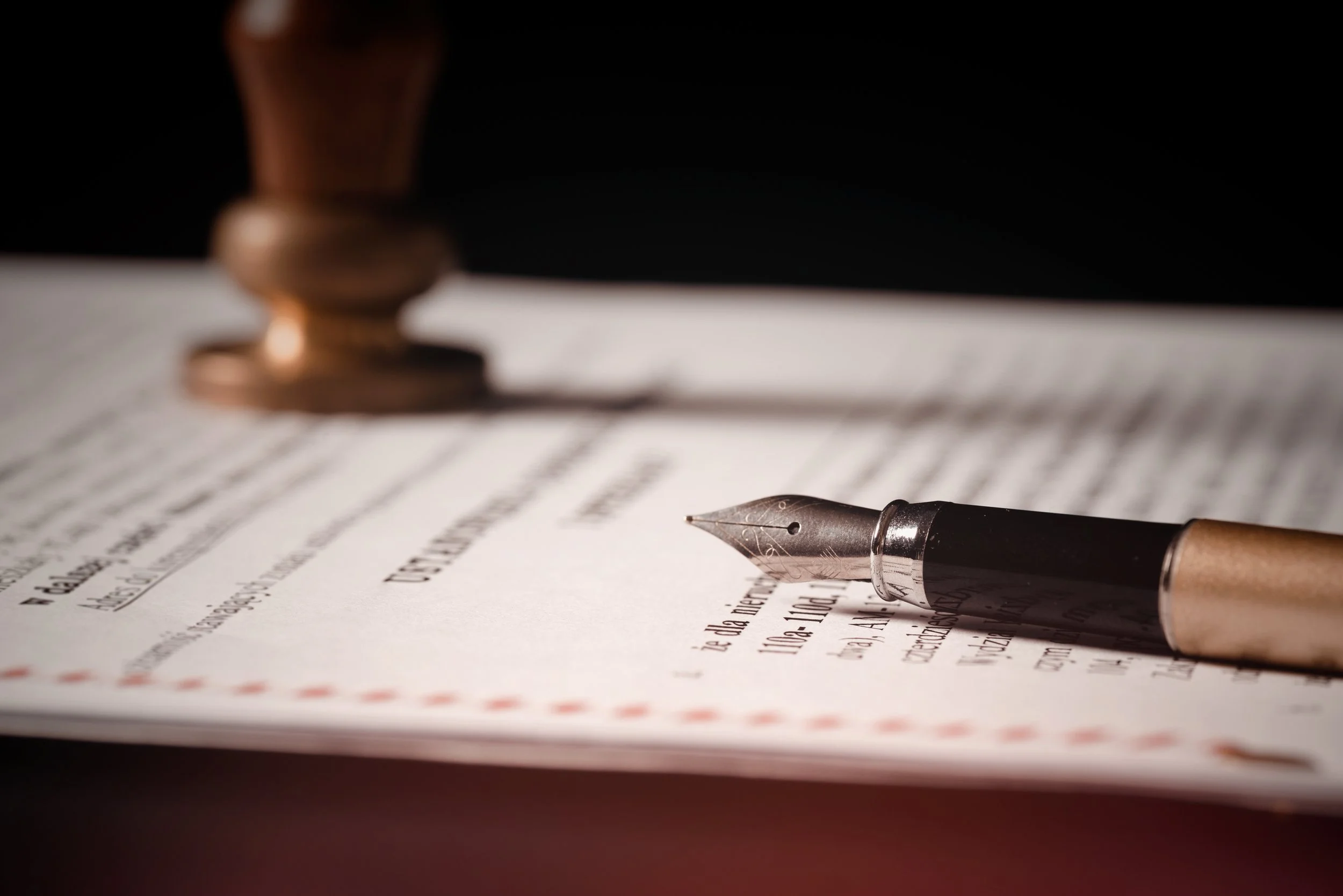 Close-up of a fountain pen resting on a legal document or contract with a gavel in the background.