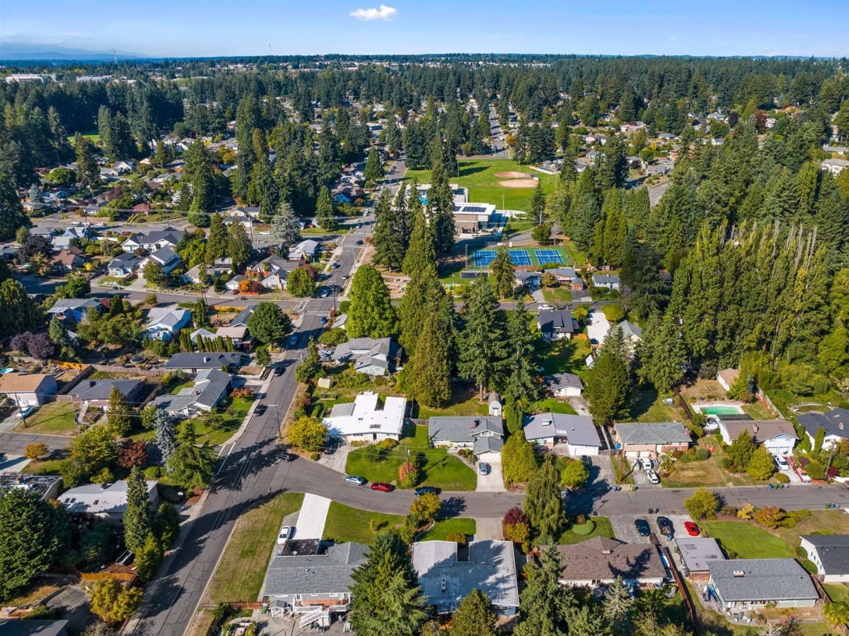 Aerial view of a suburban neighborhood with houses, trees, streets, a park with tennis and basketball courts, and many green spaces.
