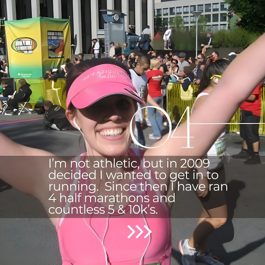 A smiling woman in a pink cap and pink running outfit at a marathon event, raising her arms in victory, with a crowd of runners and spectators in the background.