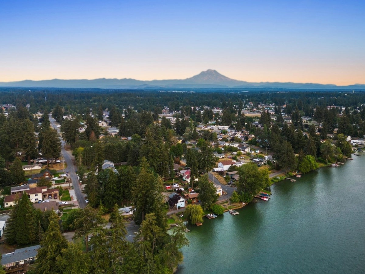 Aerial view of a lakeside residential area with houses, trees, and boats, and a distant mountain in the background during sunset.