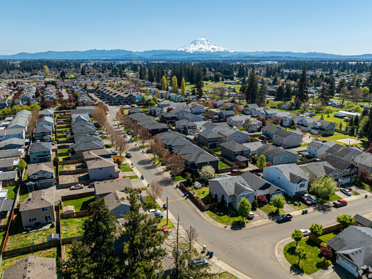 Aerial view of a suburban neighborhood with houses, trees, and streets, with Mount Hood visible in the background.