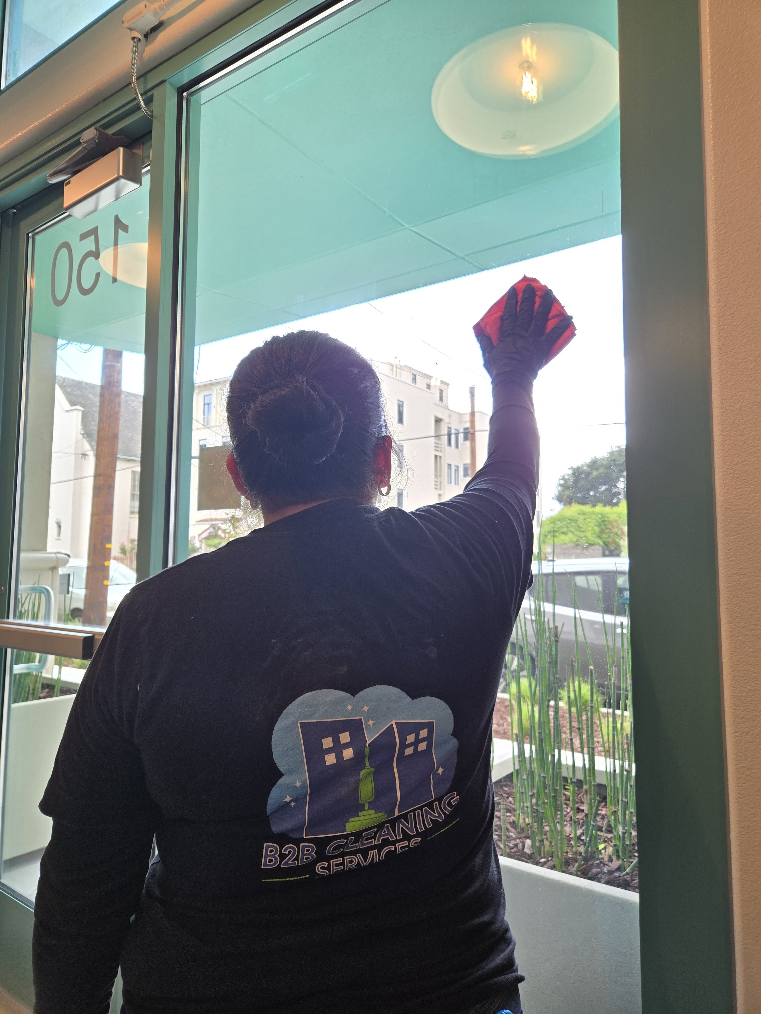 Image of a cleaning technician wearing a b2b cleaning services uniform cleaning a window at a commercial property in burlingame.
