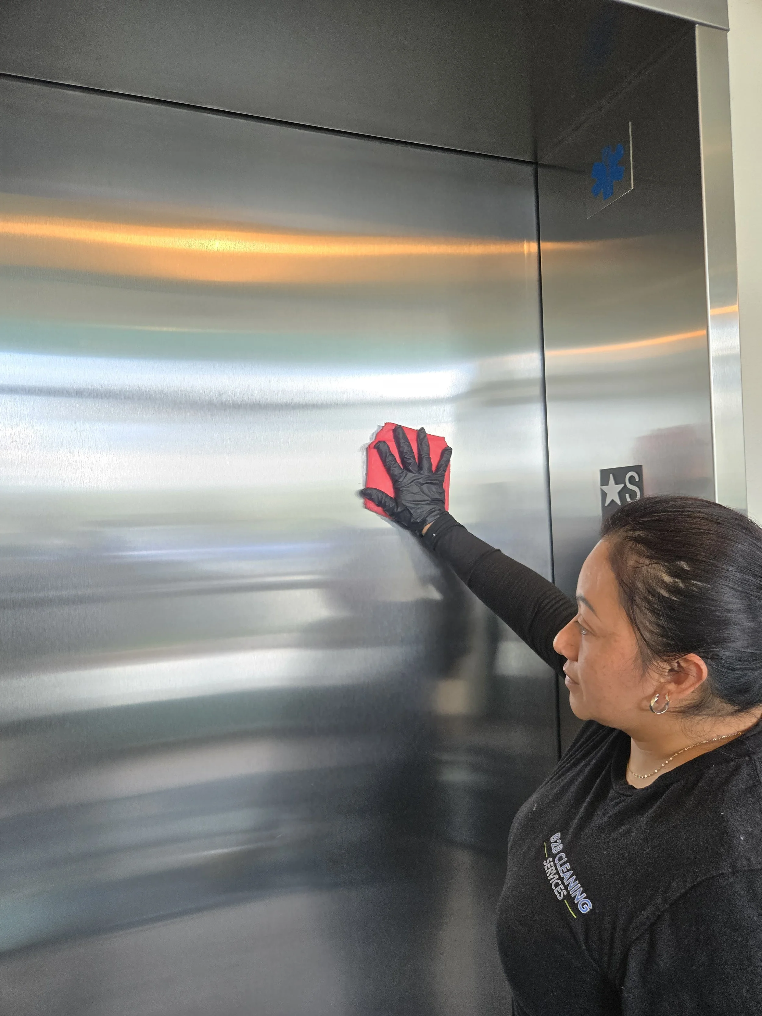 Image of a cleaning technician wearing a b2b cleaning services uniform polishing an elevator door while performing routine cleaning services for an apartment complex.