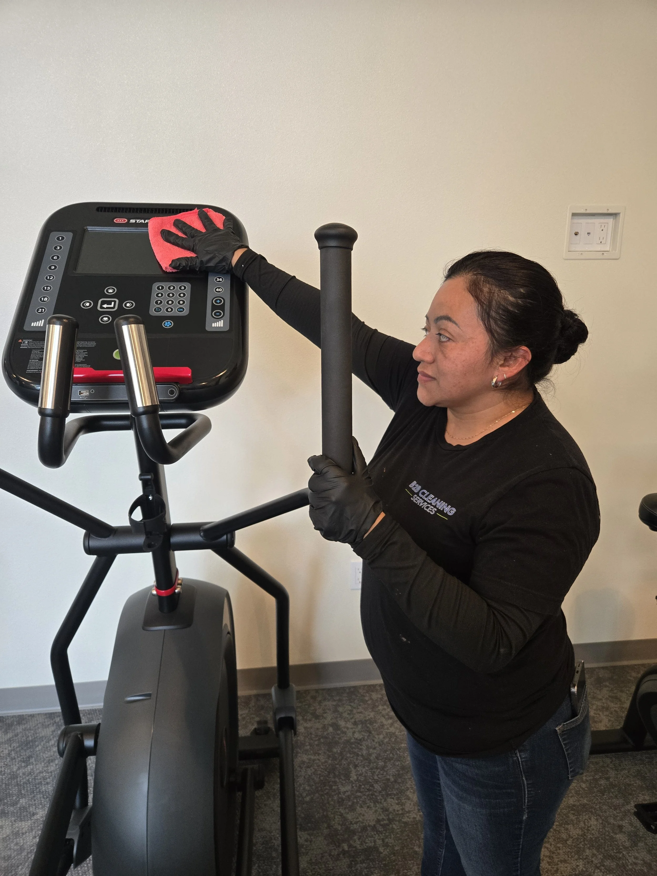 Picture of a B2B Cleaning Services cleaner providing common area cleaning services to a piece of fitness equipment in a fitness center at an apartment community.
