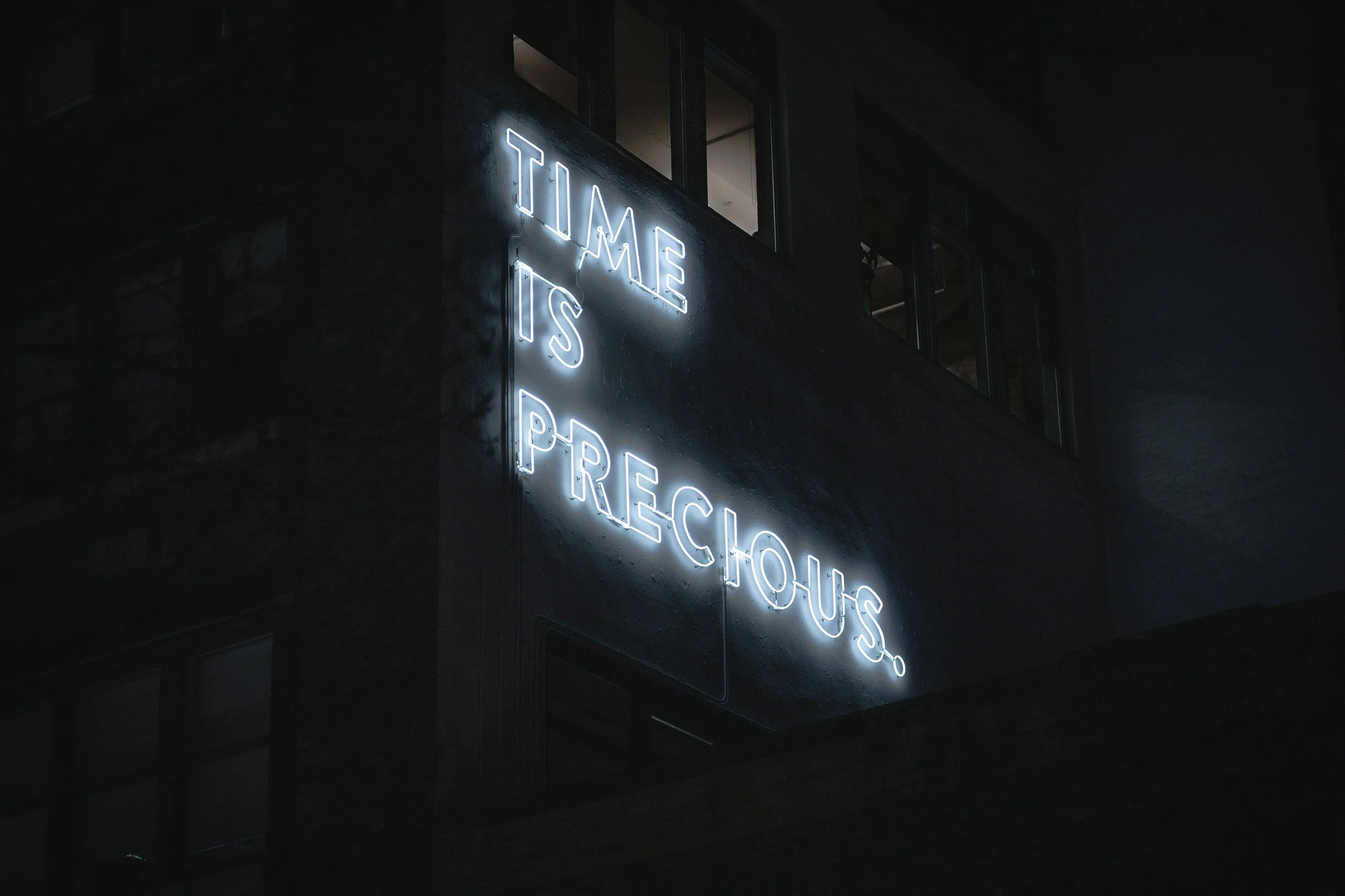 Neon sign reading ‘Time is precious’ on building at night representing time-saving bookkeeping services