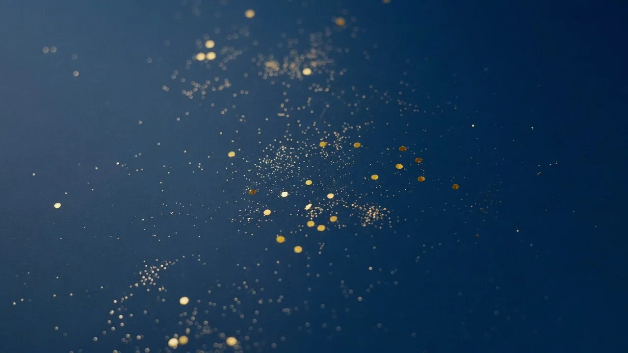 Close-up of small gold and white glitter particles scattered on a dark blue surface.