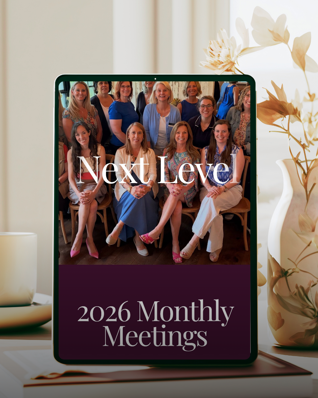 A tablet displaying a group photo of smiling women at a meeting with text overlay reading 'Next Level' and '2026 Monthly Meetings.' The tablet is on a desk next to a white vase with dried flowers.