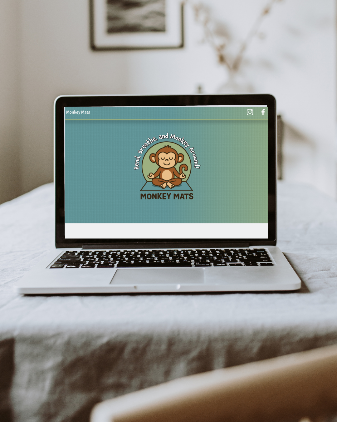 Laptop on a bed displaying a logo with a cartoon monkey meditation icon and the text 'Bend, Breathe, Breathe, and Monkey Around! MONKEY MATS'.
