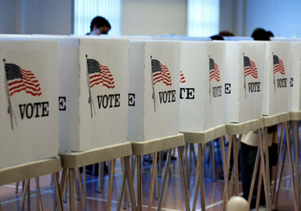 Voting booths with American flags and 'VOTE' signs in a polling station.