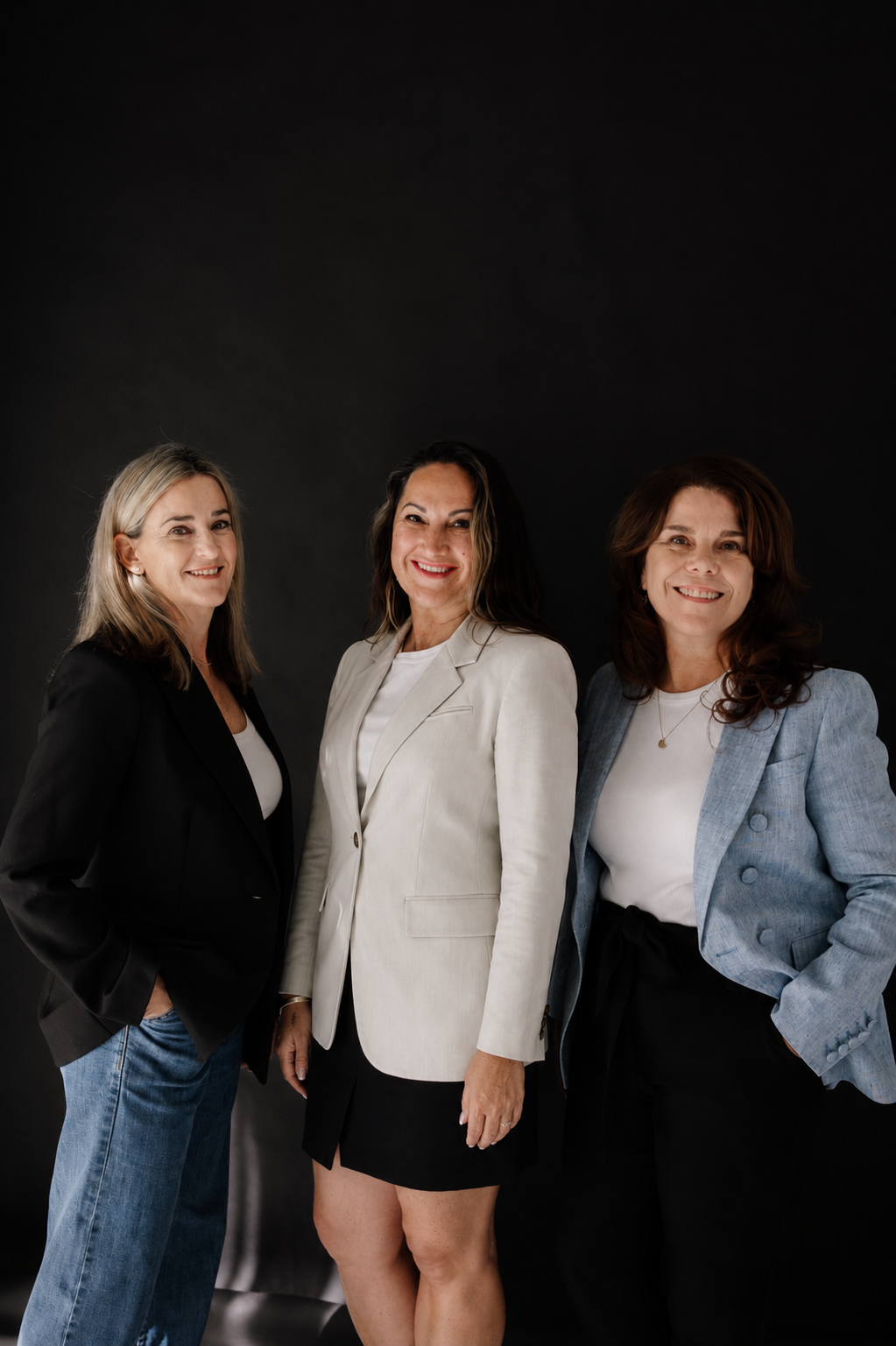 Three women in professional attire smiling against a black background.